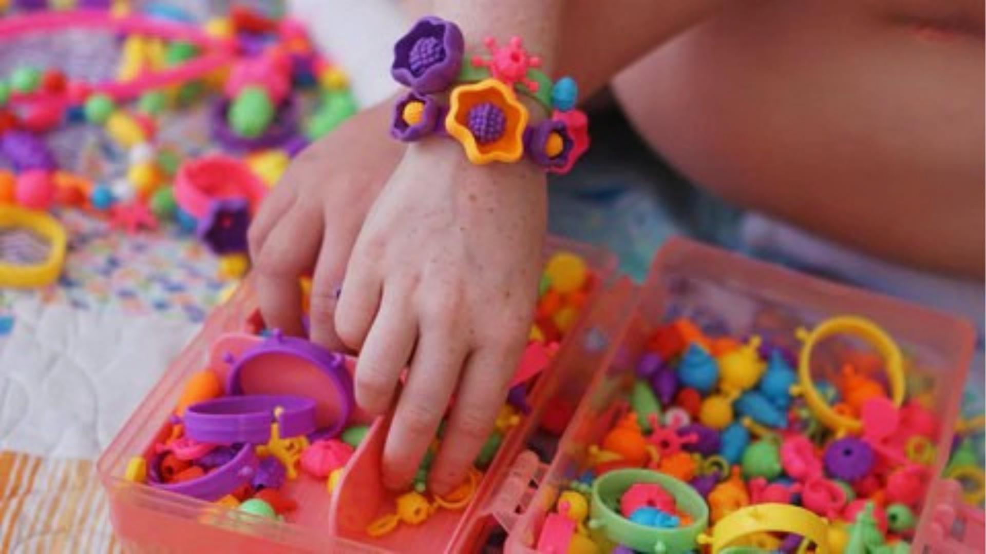 Child selects bright plastic beads and bracelets from pink containers, wearing flower bracelets, crafty.