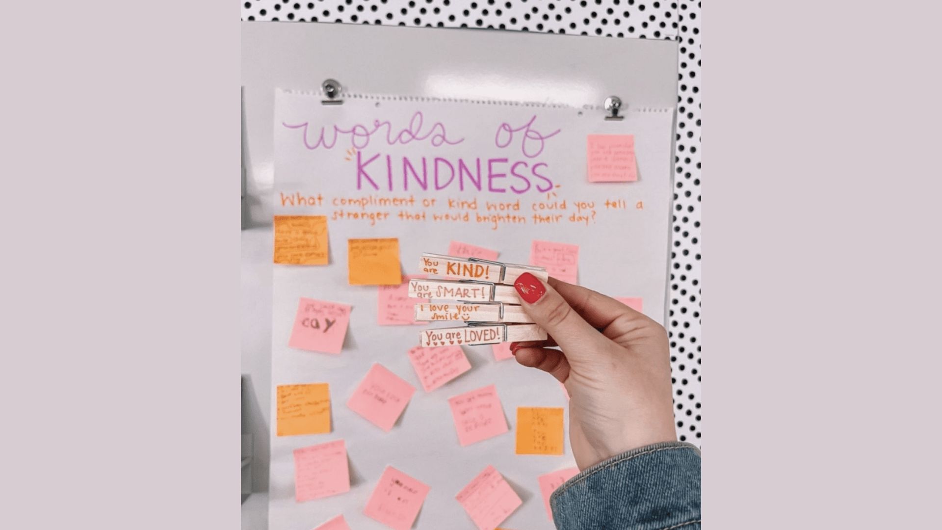A “Words of KINDNESS” classroom chart with pink and orange sticky notes and a hand holding clothespins labeled notes.