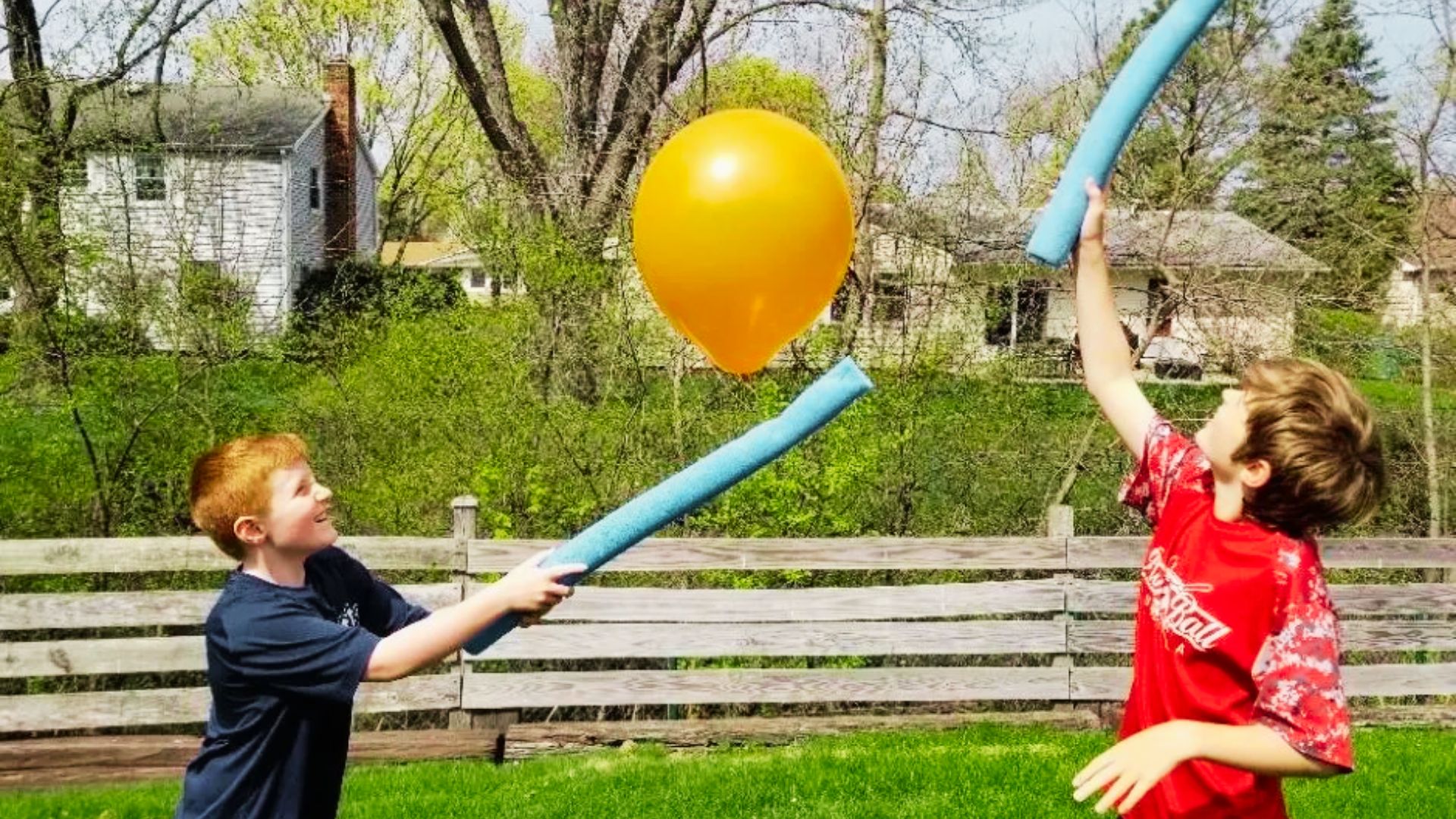 Two boys joyfully playing with a colorful balloon and a stick in a grassy field.