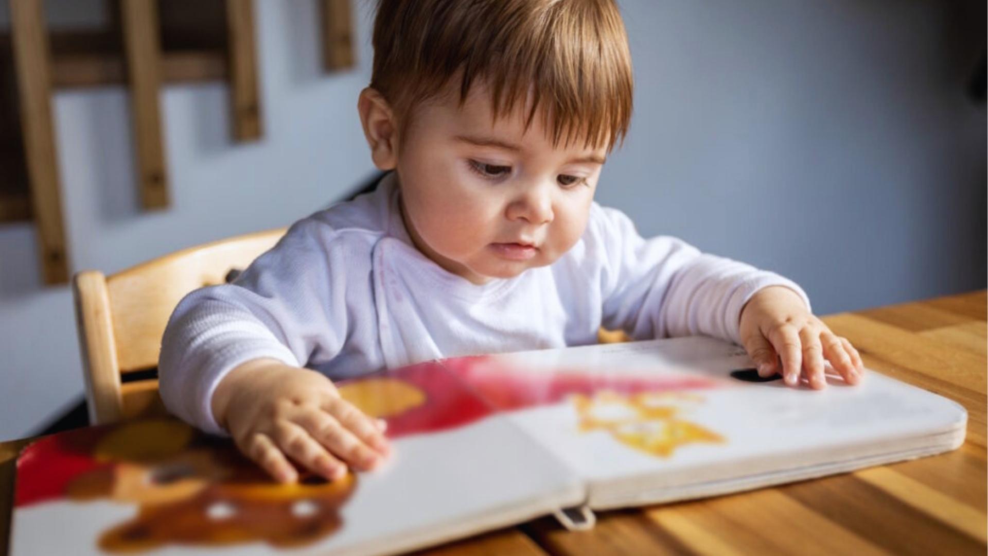 Toddler in white shirt find textured board book at table, sensory reading time, Activities for Autistic Kids.