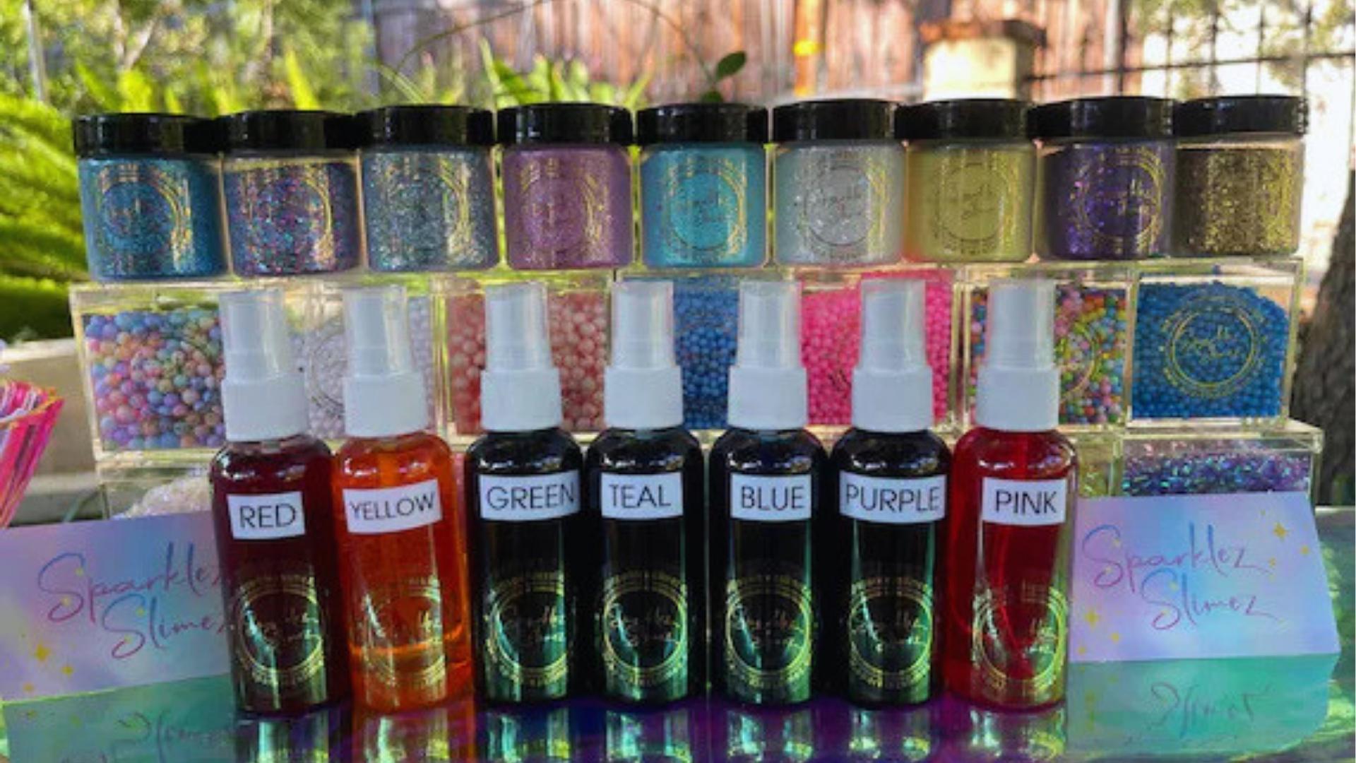 Jars of glitter and beads, bottles labeled RED to PINK, slime making station, outdoors.