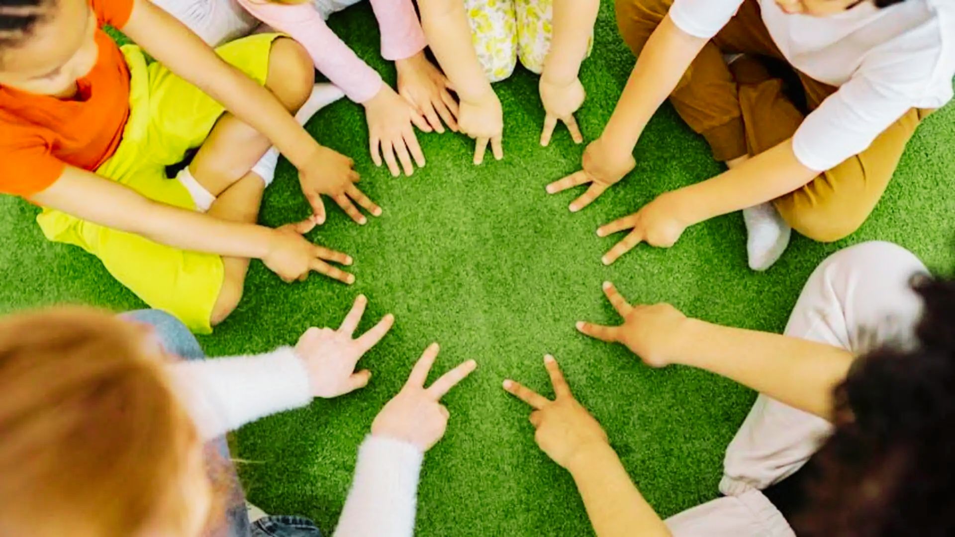 A group of children sitting in a circle on green grass, engaged in a playful activity together.