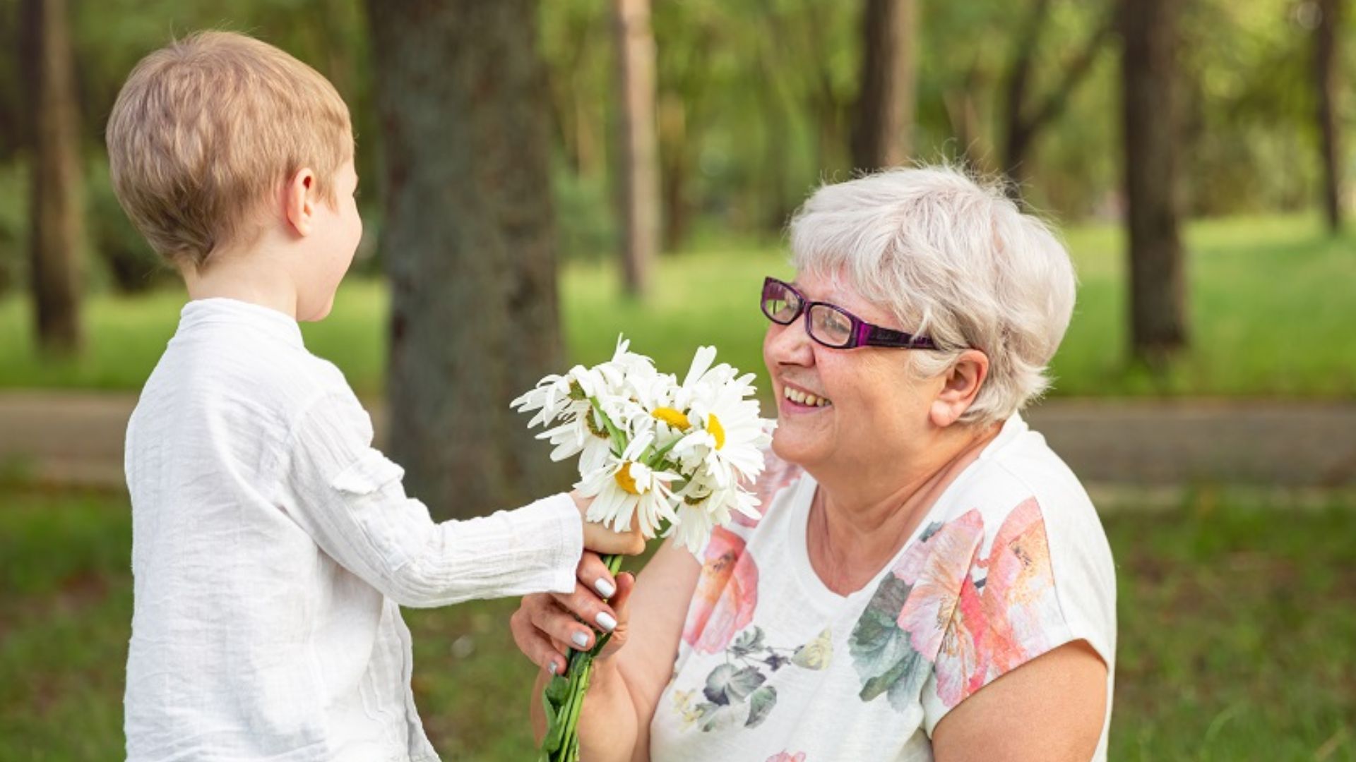 Young boy giving a bouquet of daisies to his smiling grandmother to practice kindness and empathy, a self esteem activity for kids that builds confidence through giving