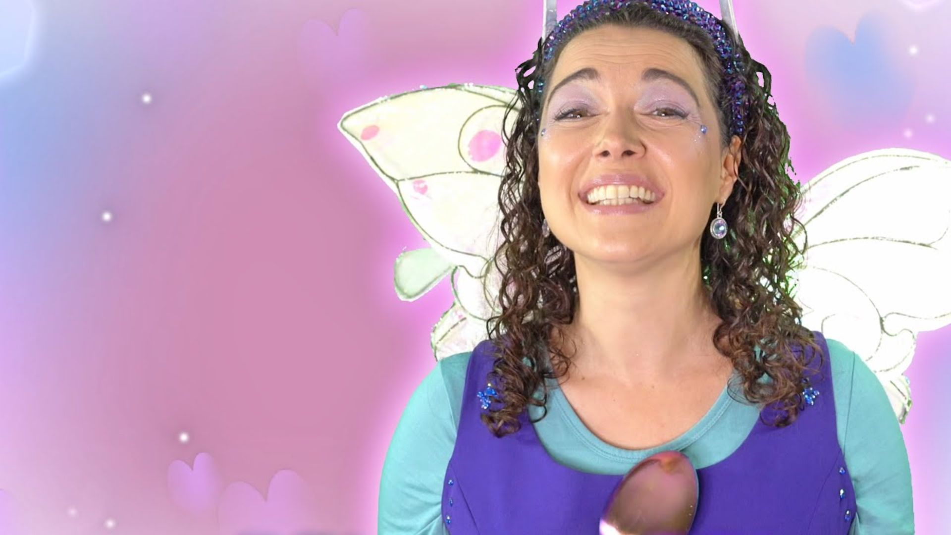 A smiling woman dressed as a kind fairy with butterfly wings and a purple costume for a bucket filler lesson.