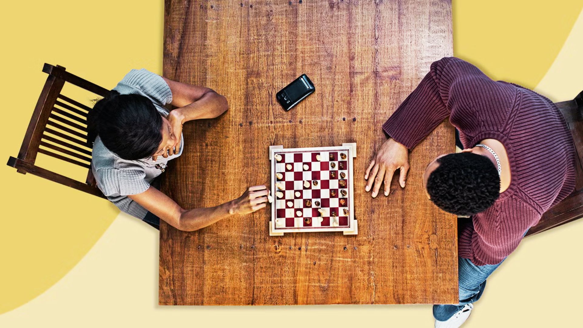 Two men engaged in a chess game, focused on the board, seated at a wooden table.