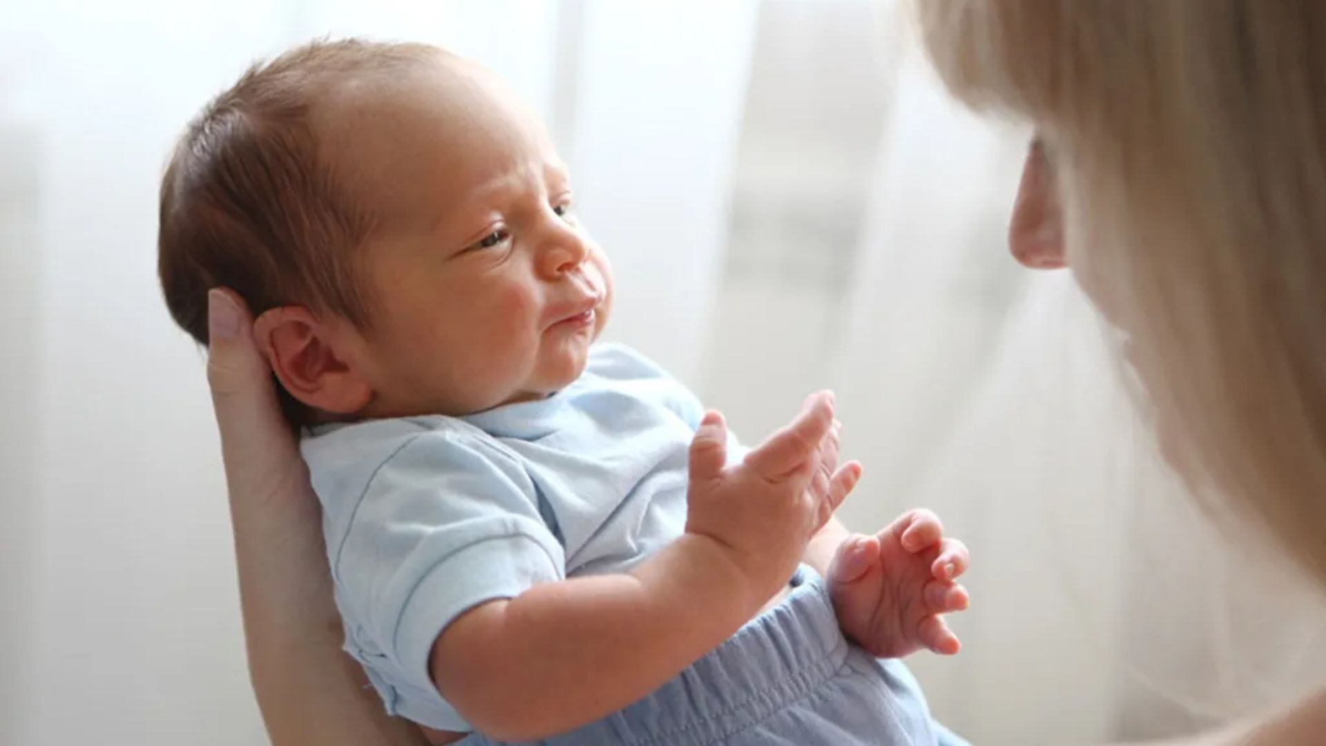 Close-up of proper head and neck support: Adult's hand cradles a newborn's head and neck while holding the baby, critical for infants under 3 months.