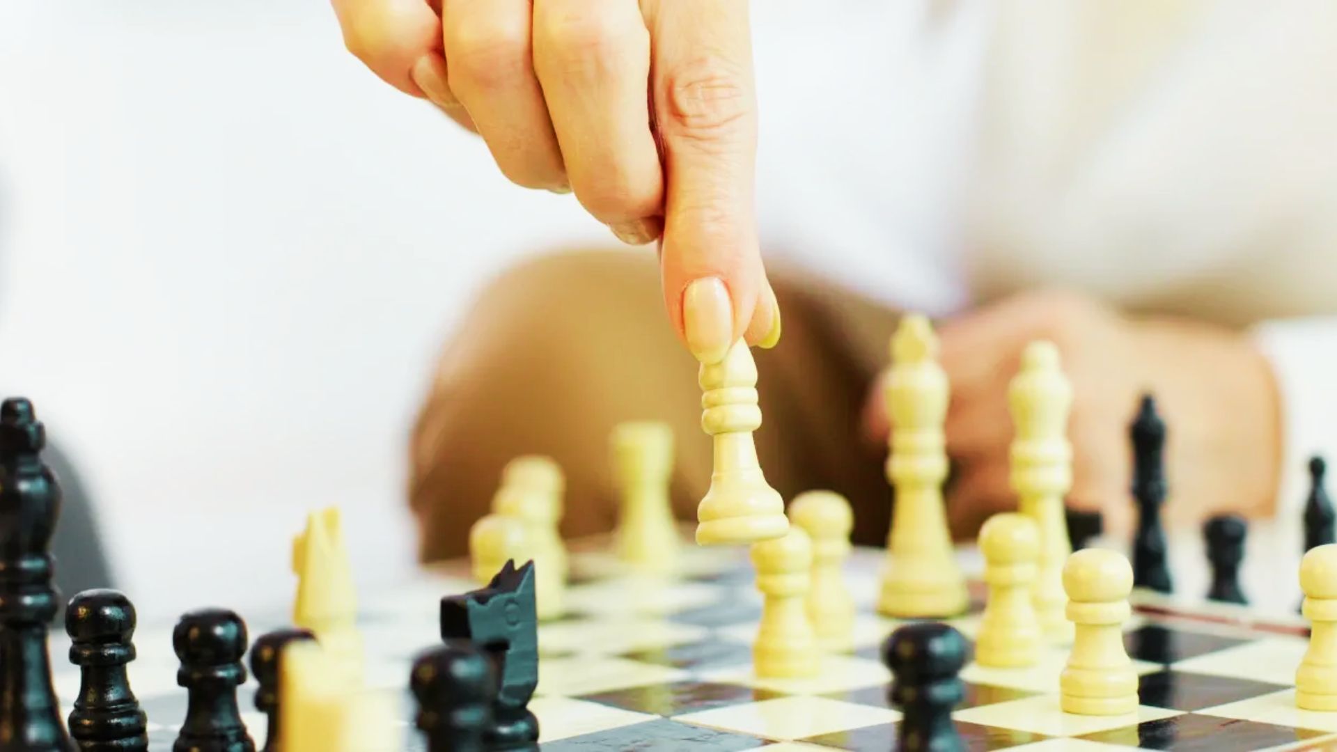 A person thoughtfully plays chess, moving a piece on the board during a problem-solving activity for teens.