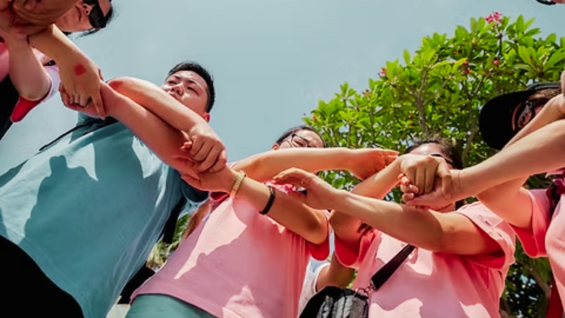 A group of people wearing pink and green shirts, standing in a circle and holding hands together in solidarity.