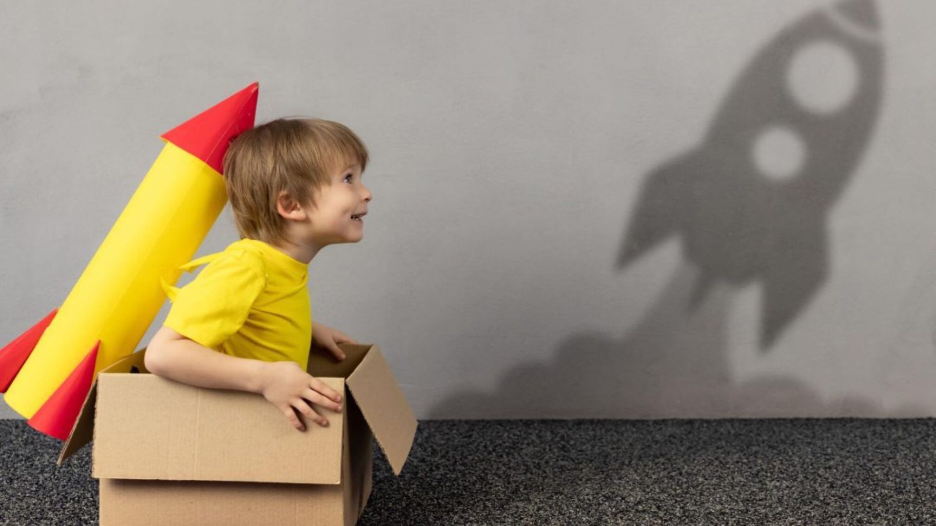 A child enjoys sitting in a cardboard box designed as a rocket, participating in creative role-play activities.