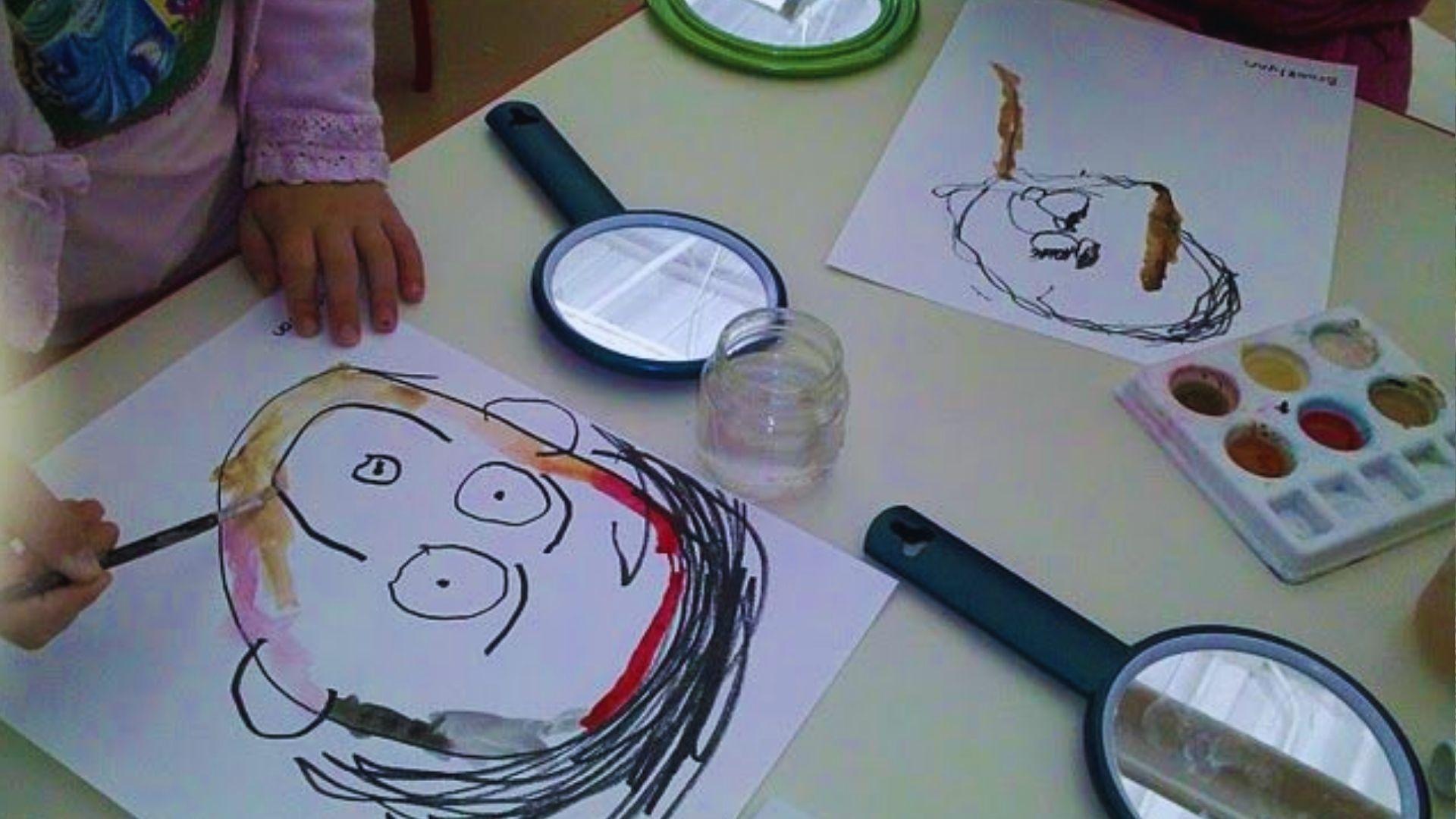 Children engaged in an art activity, using a magnifying glass to examine details in their artwork.