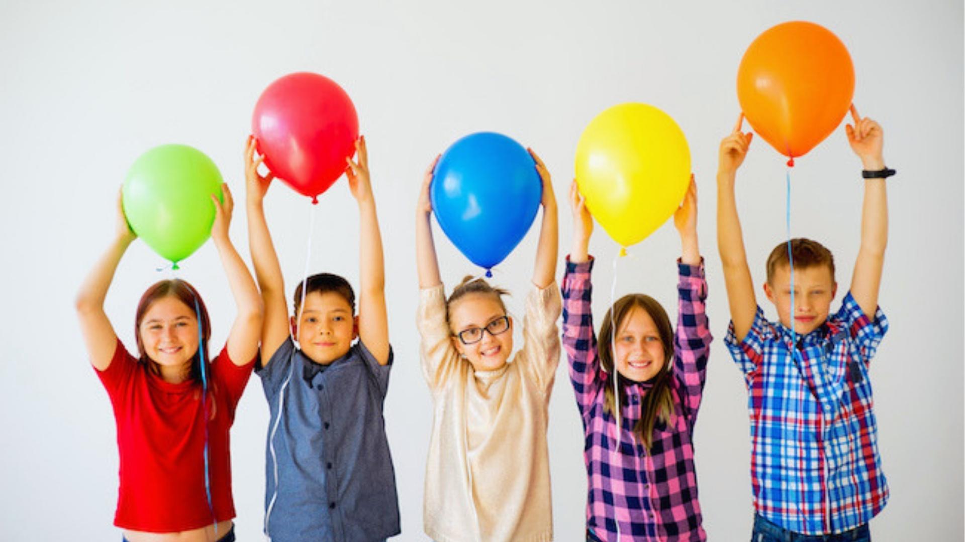 Five happy kids holding colorful balloons overhead, white background, celebrating together, smiling brightly.