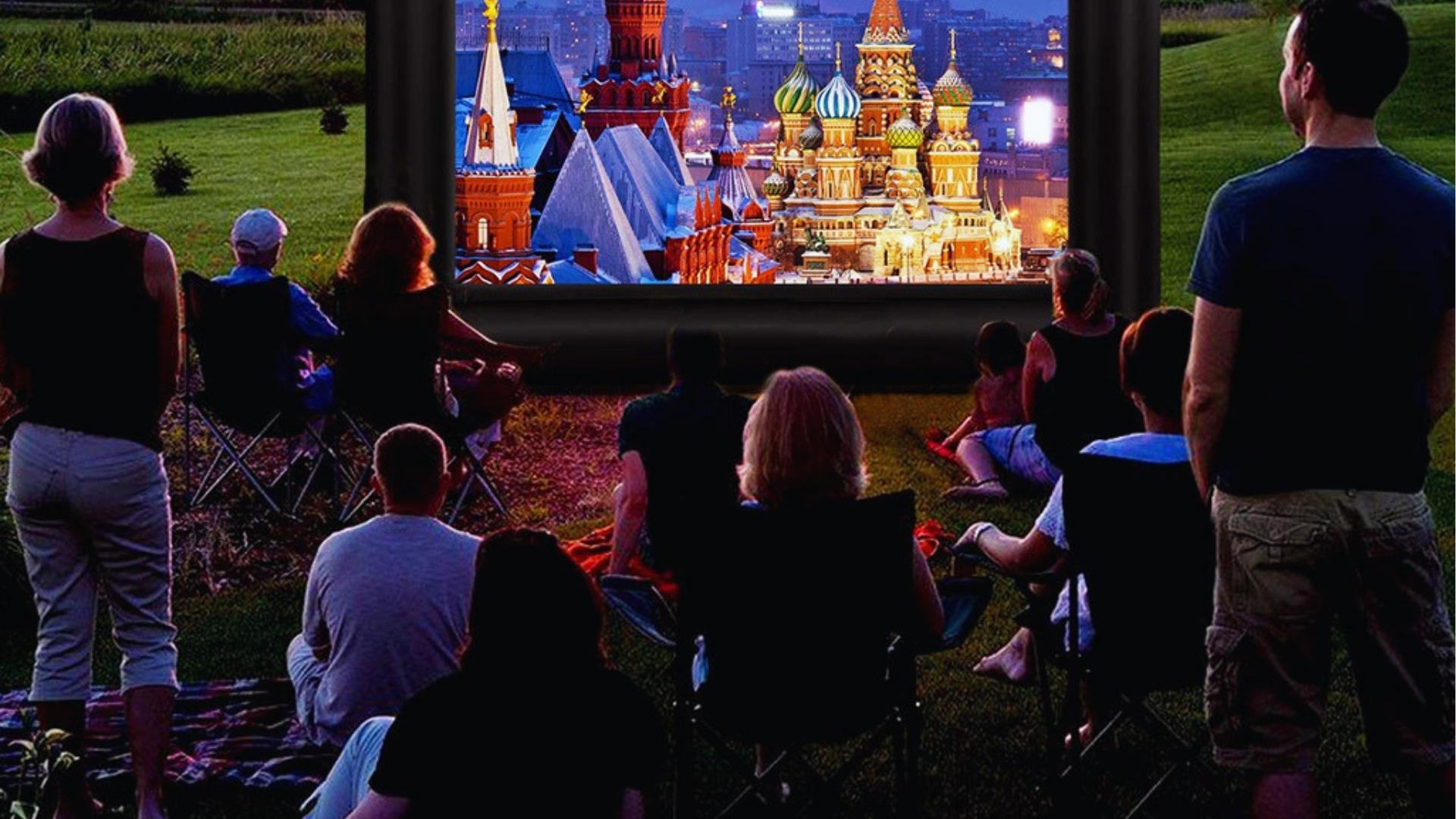 Family watching outdoor movie on inflatable screen at dusk, lawn chairs, blanket.