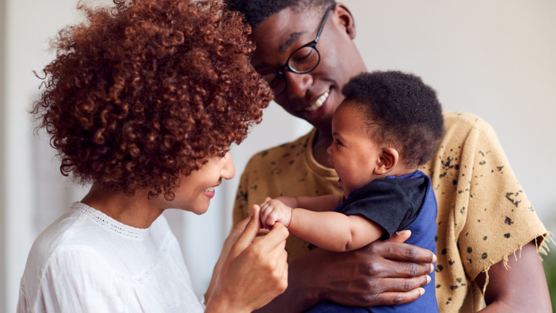 Parents demonstrate the upright hold together. Father supports the baby's head, back, and bottom against his chest while maintaining eye contact.