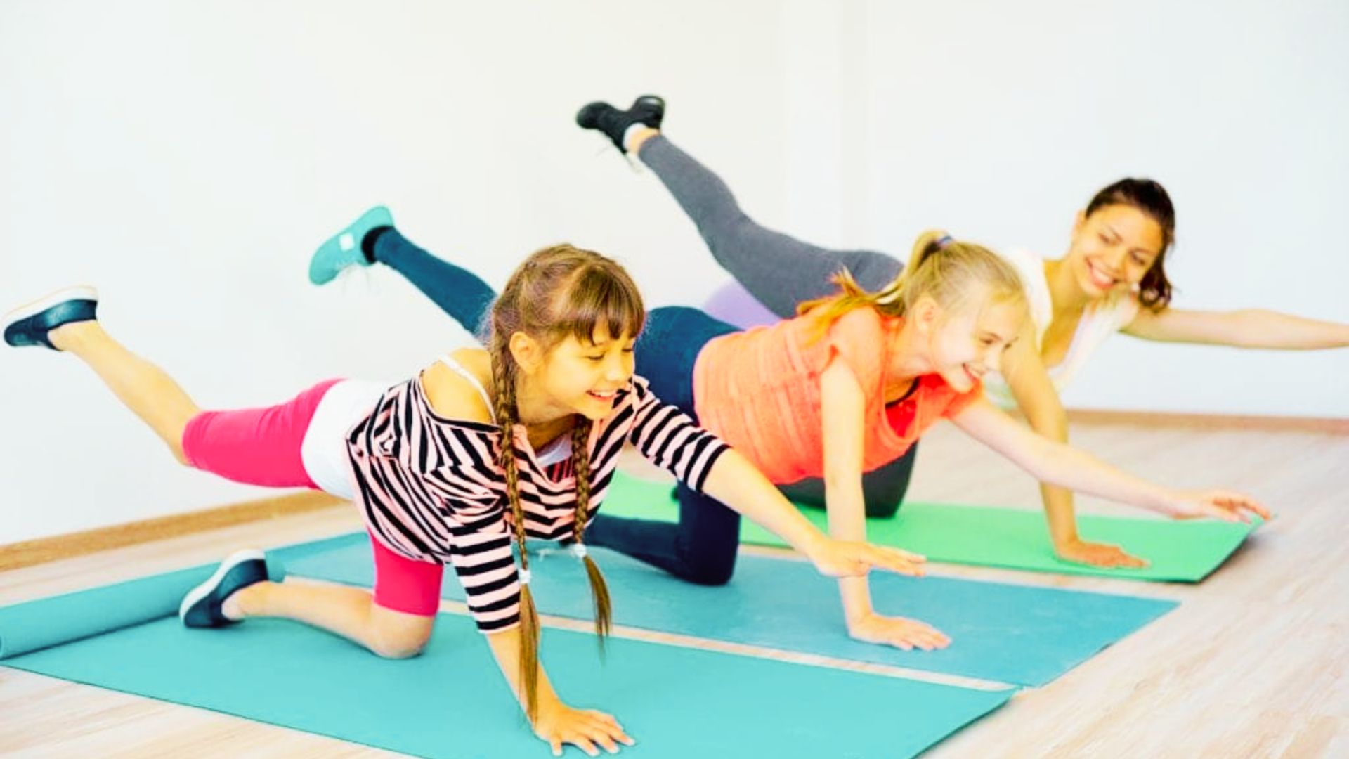 Three girls practicing yoga poses on a colorful mat in a serene indoor setting.