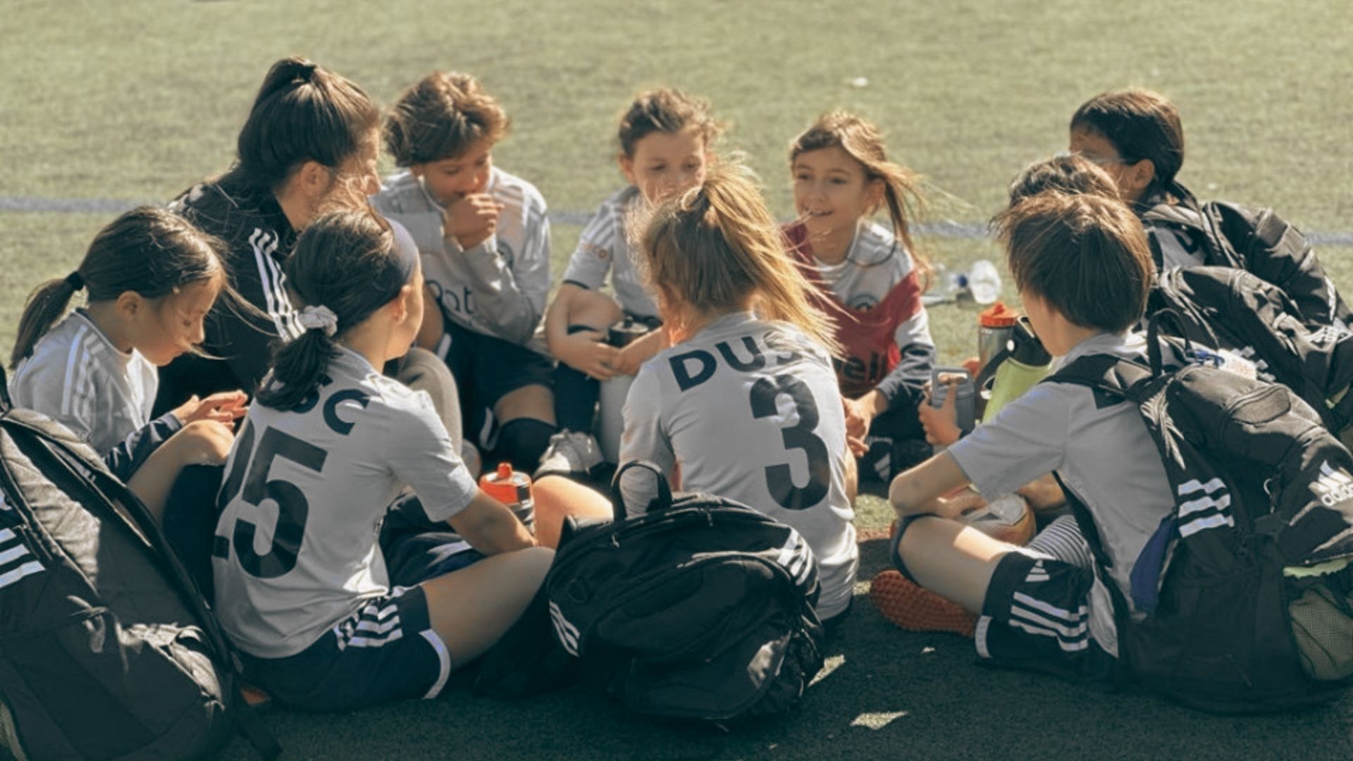 A group of young girls and boys sitting on the ground, engaged in conversation and enjoying each other's company.