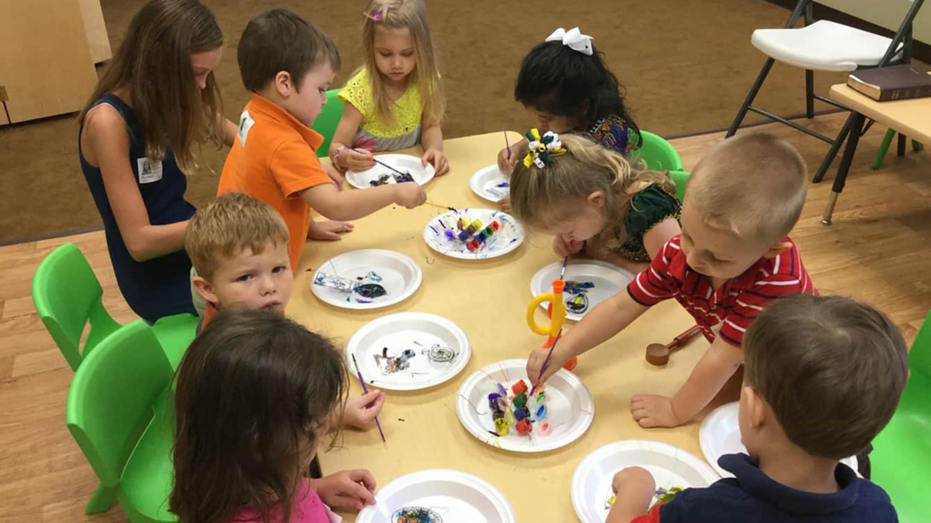 Group of preschoolers sitting together painting on paper plates, sharing art supplies and creating side by side in a collaborative friendship activity for kids