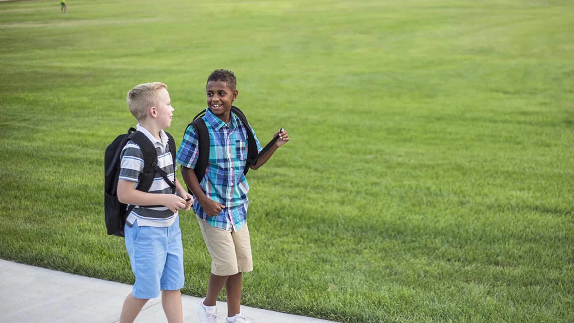 Two preschool boys with backpacks walking side by side and talking on a school path, showing peer connection and conversation skills in a friendship activity for kids