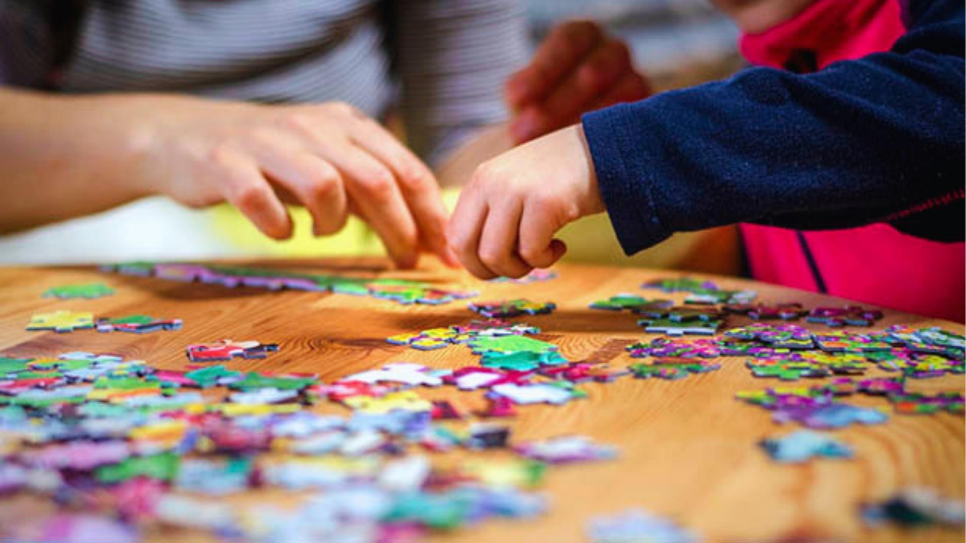 Close up of childโs hands assembling colorful jigsaw puzzle pieces on wooden table.