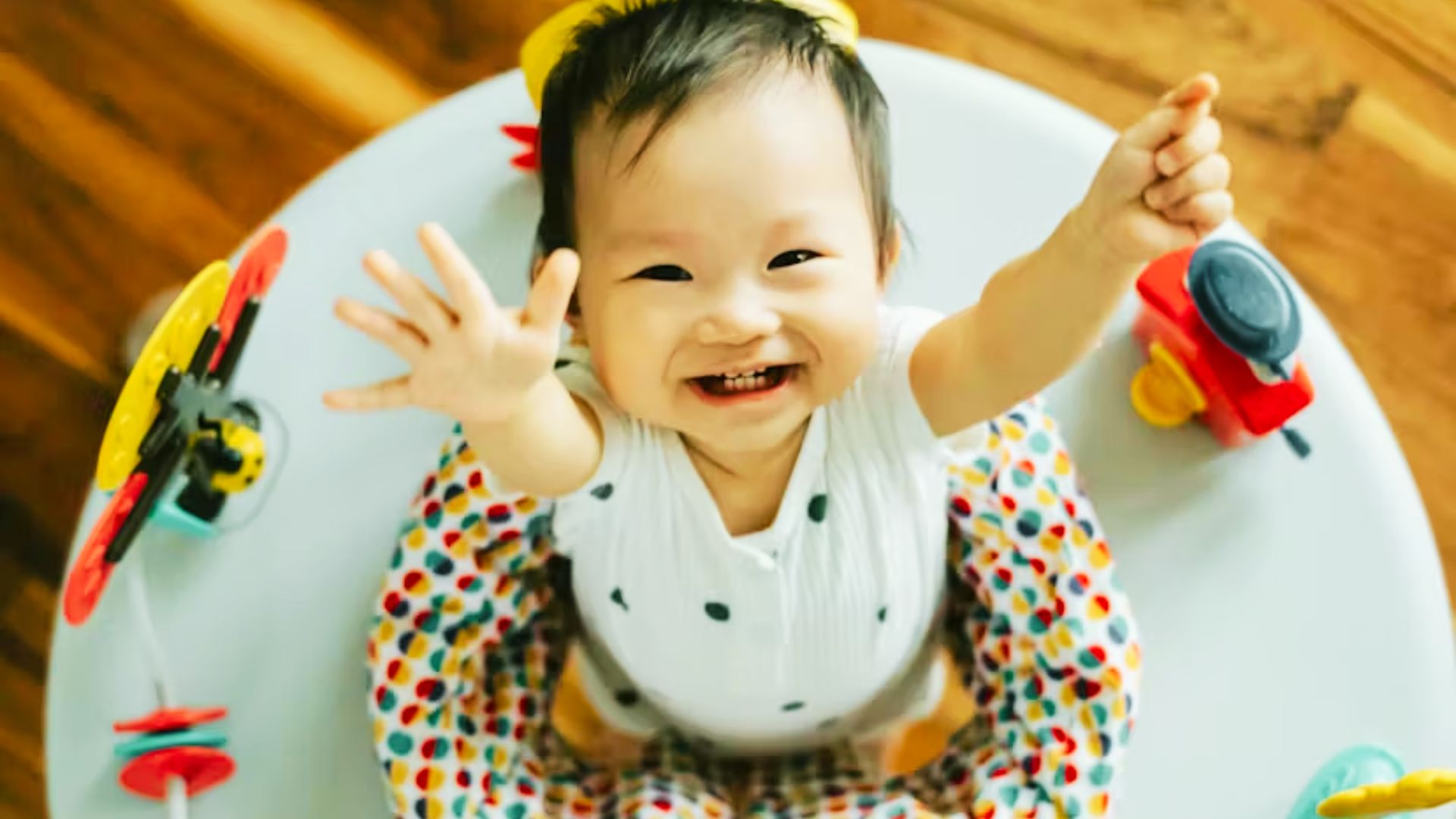 A baby sits on a colorful toy in a vibrant play area filled with soft mats and various toys.