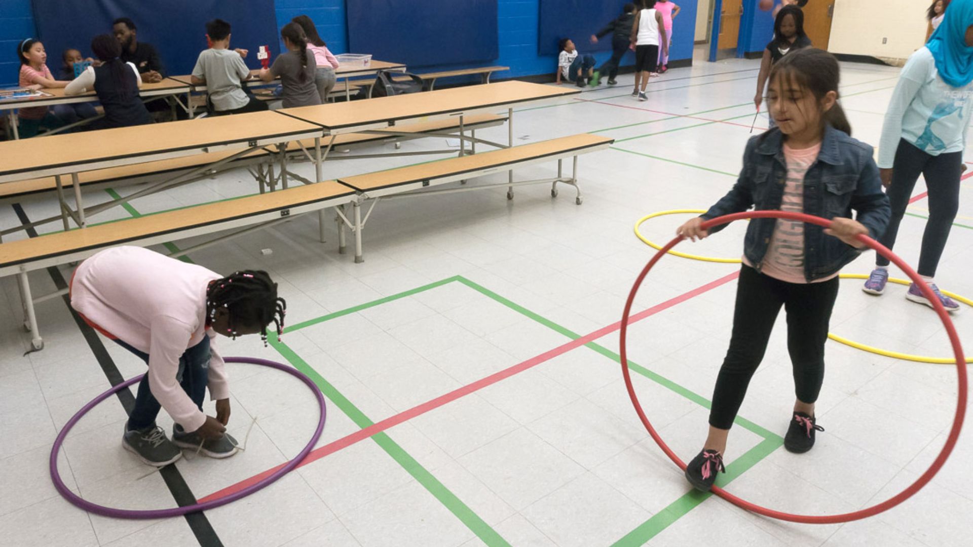 Alt text: Students standing and moving between two circles marked on a classroom floor while a teacher guides an interactive activity