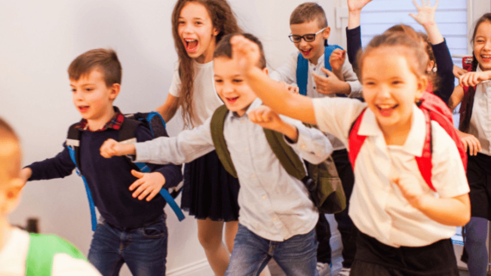 Excited group of preschoolers with backpacks running and playing together indoors, demonstrating joyful group play and social bonding as a friendship activity
