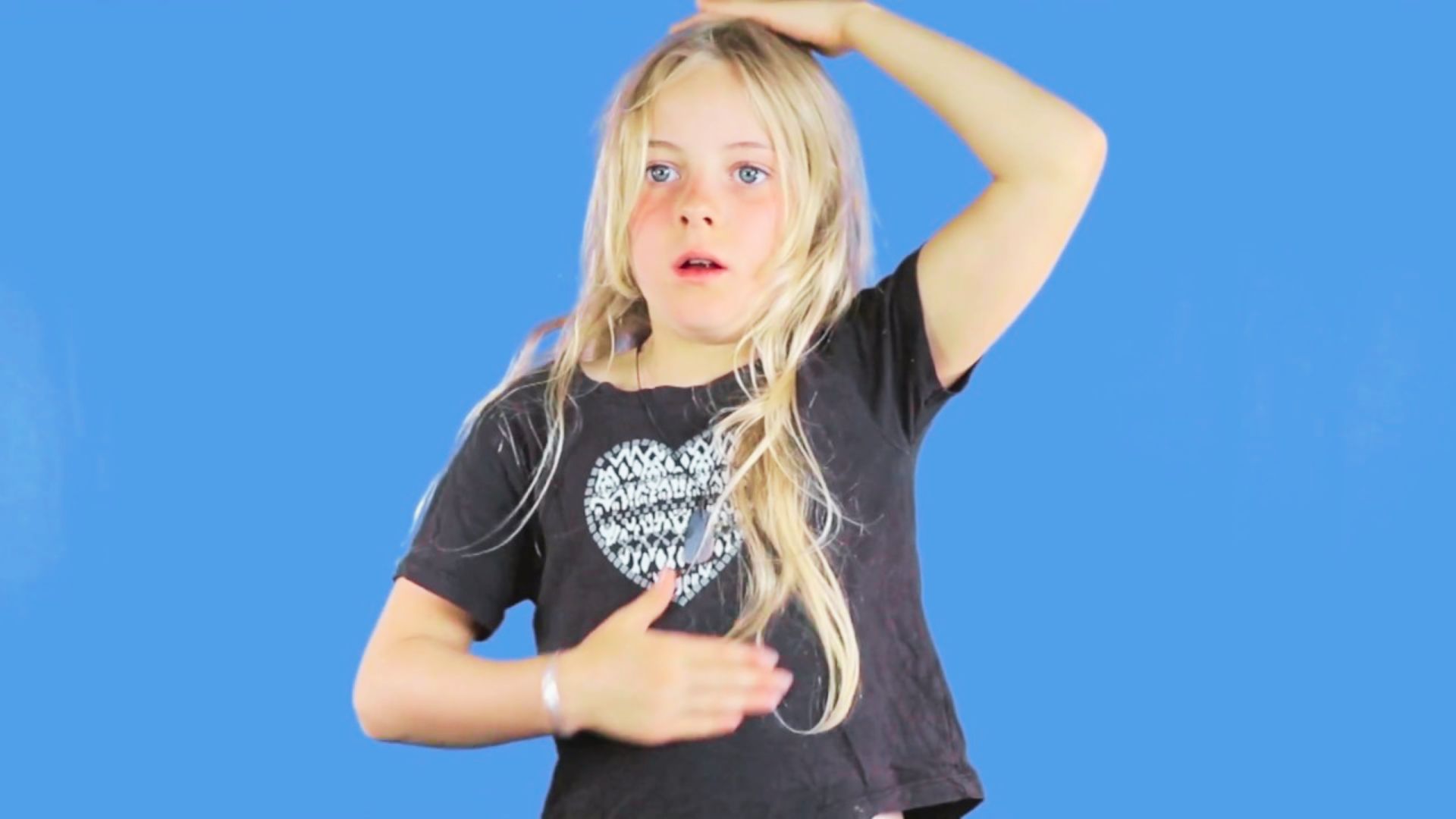 A young girl with long hair wearing a black shirt, smiling and looking towards the camera.