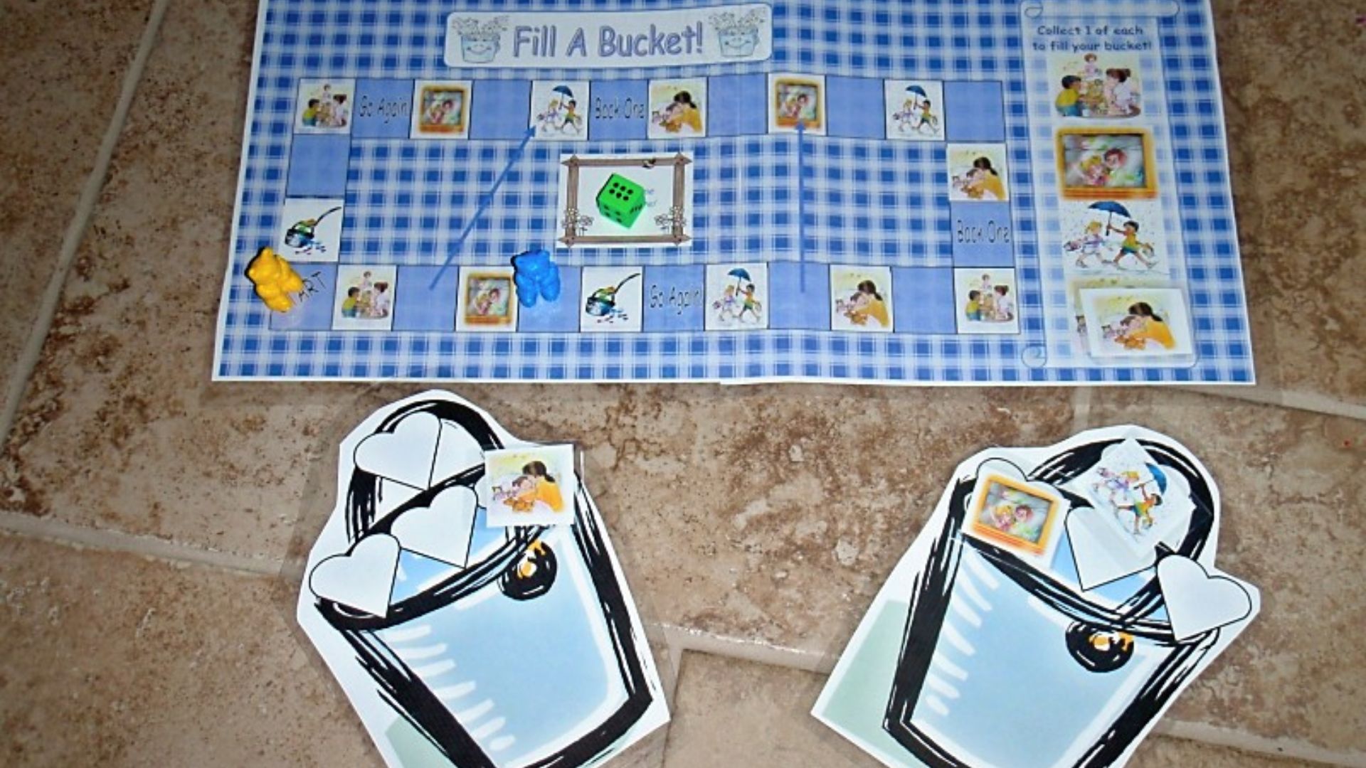 DIY “Fill A Bucket!” board game for kids with a blue gingham game board, green die, teddy bear game pieces, and paper buckets to collect picture cards.