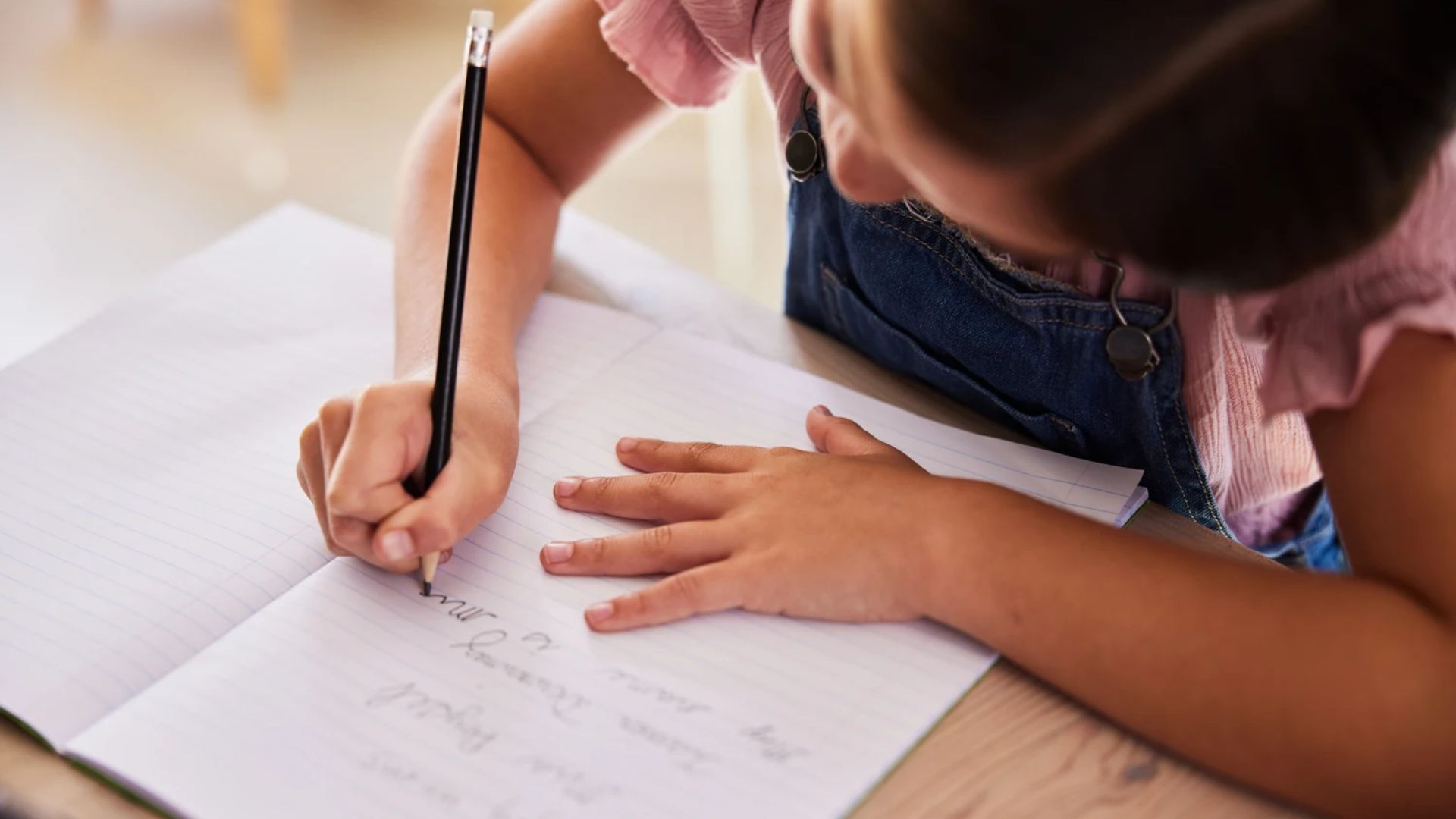 Child writing in a journal on a wooden desk, illustrating a self esteem activity for kids focused on positive self talk and recognizing personal strengths