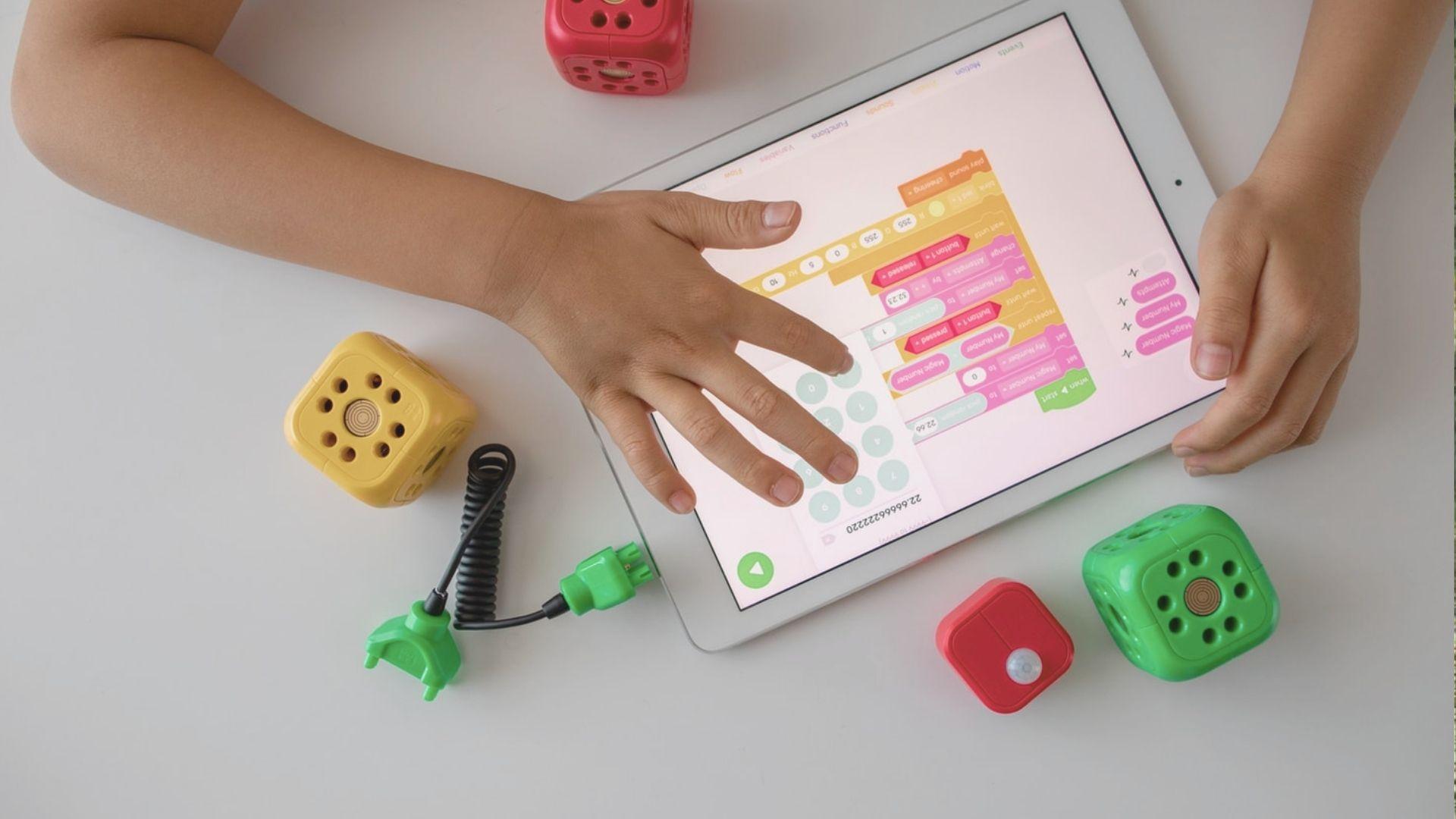 A child sits on the floor, focused on a tablet while surrounded by colorful building blocks.