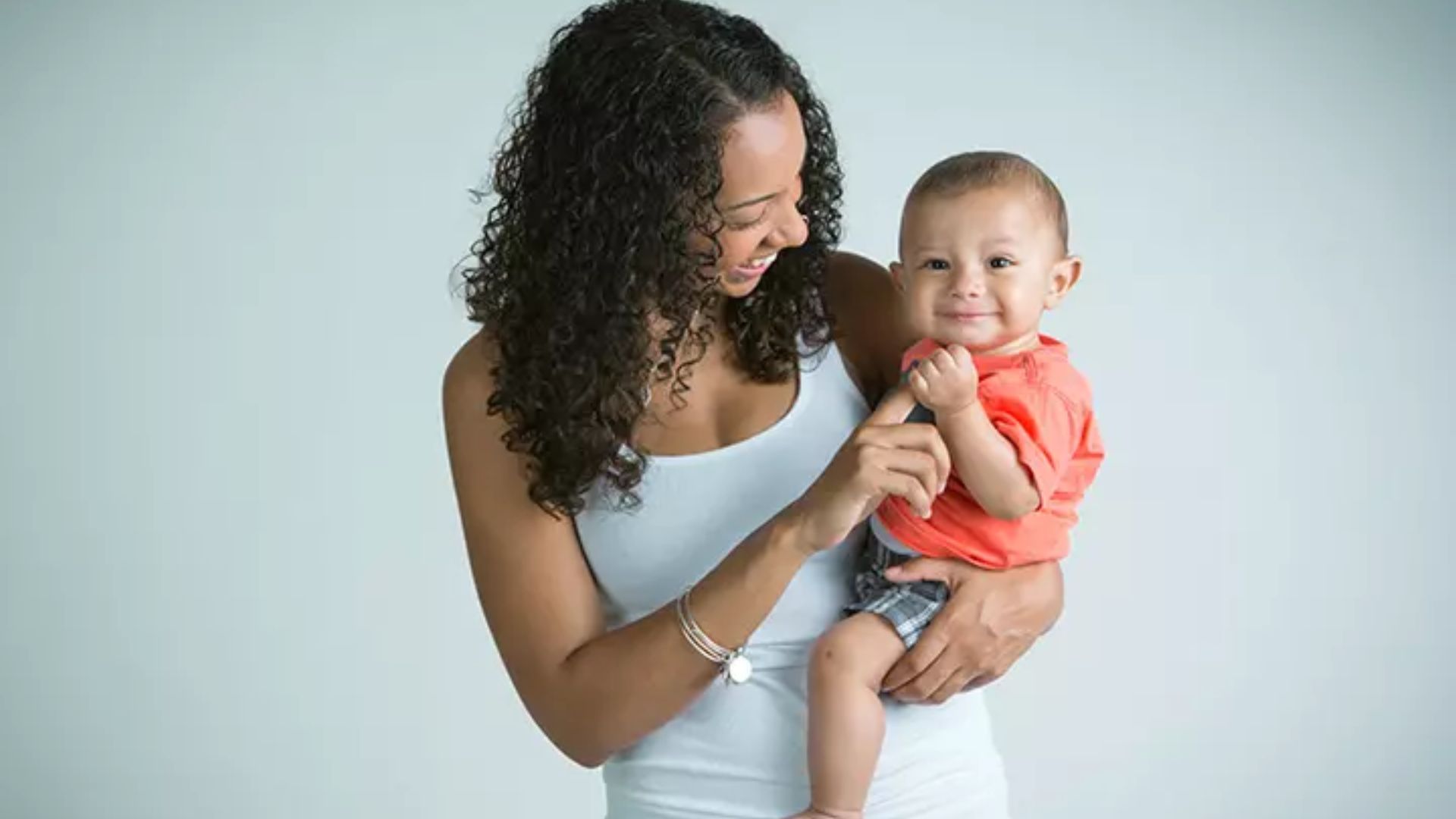 Mother demonstrates the hip hold for older babies. The baby sits upright on her hip with head control, secured by an arm around the back.