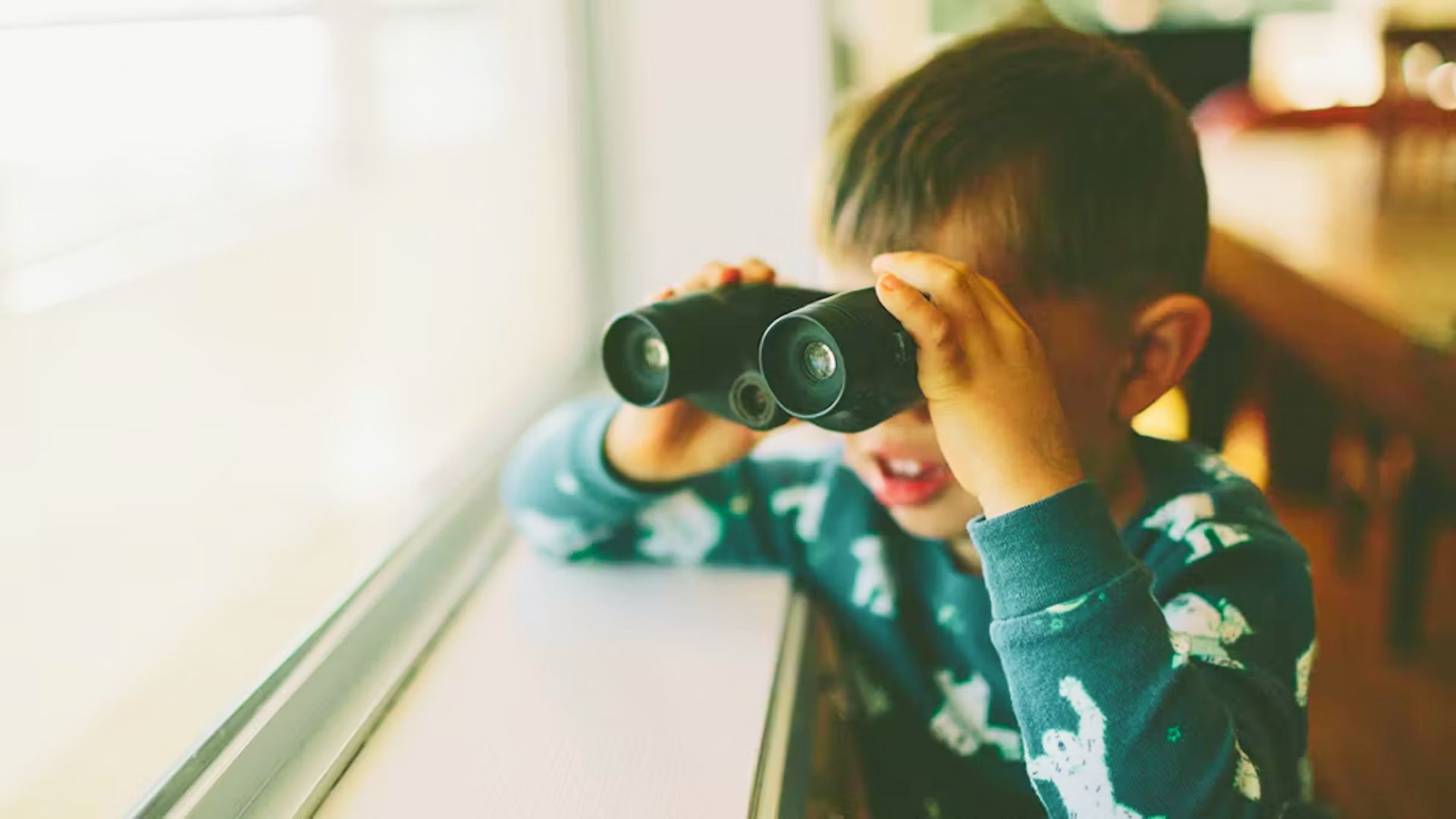 A young boy gazes through binoculars, focused on something in the distance, with a look of curiosity on his face.