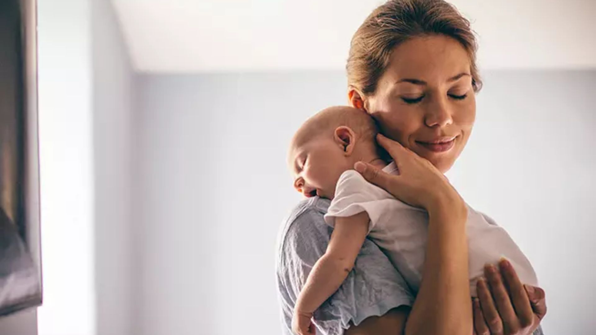 Mother demonstrating the shoulder hold for comfort or burping: Baby faces inward with chin resting on shoulder, while adult supports the head and back with one hand.