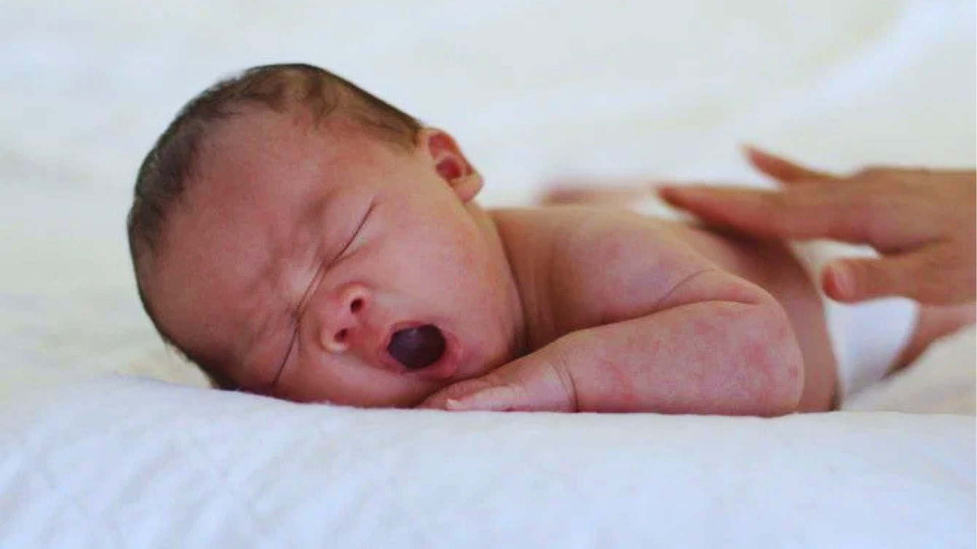 Newborn baby yawning while lying down, as head shaking side to side is common when infants are tired or self-soothing