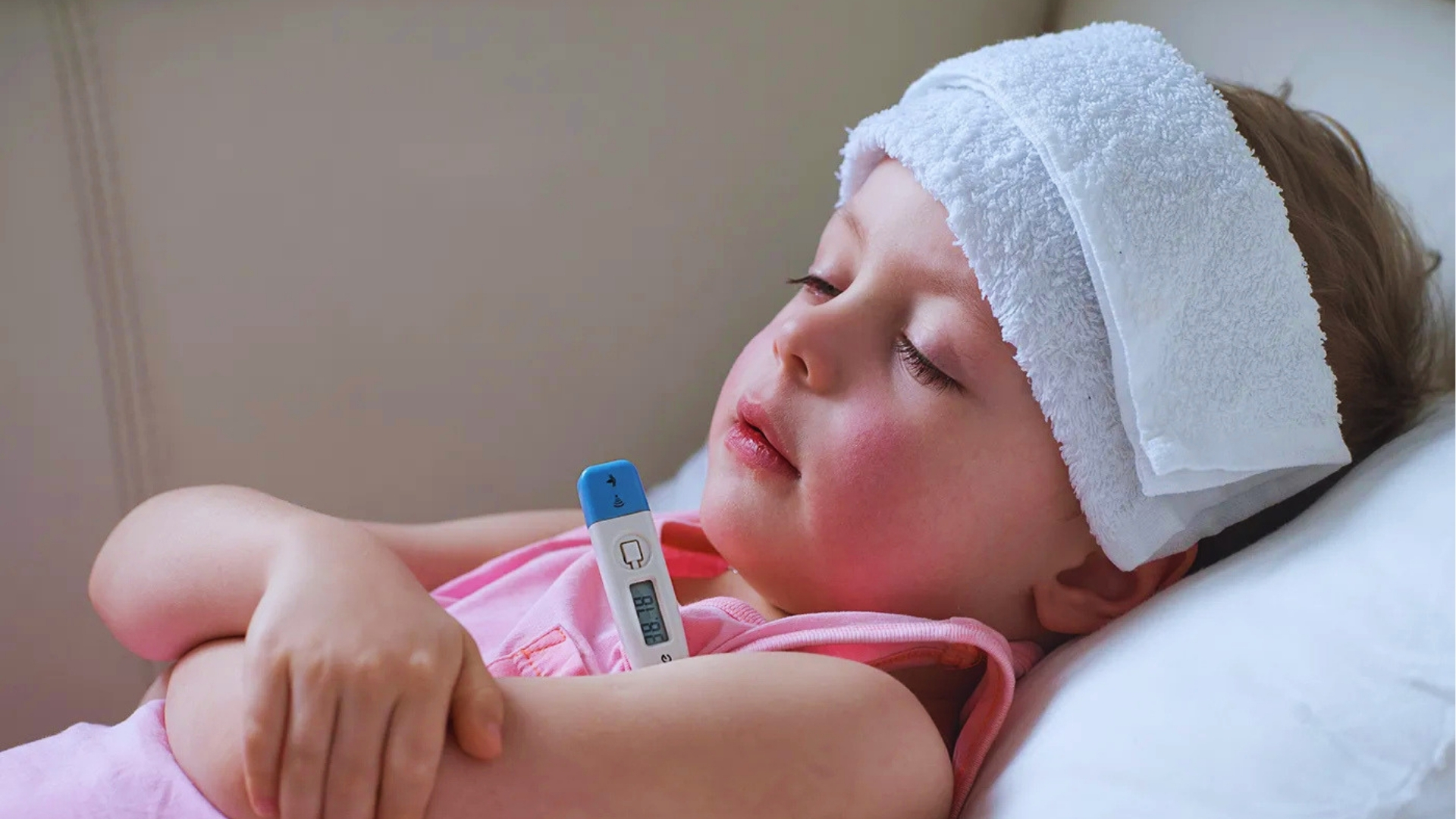 Young child with fever lying down with wet towel on head and thermometer, showing common home care for nighttime toddler fever.
