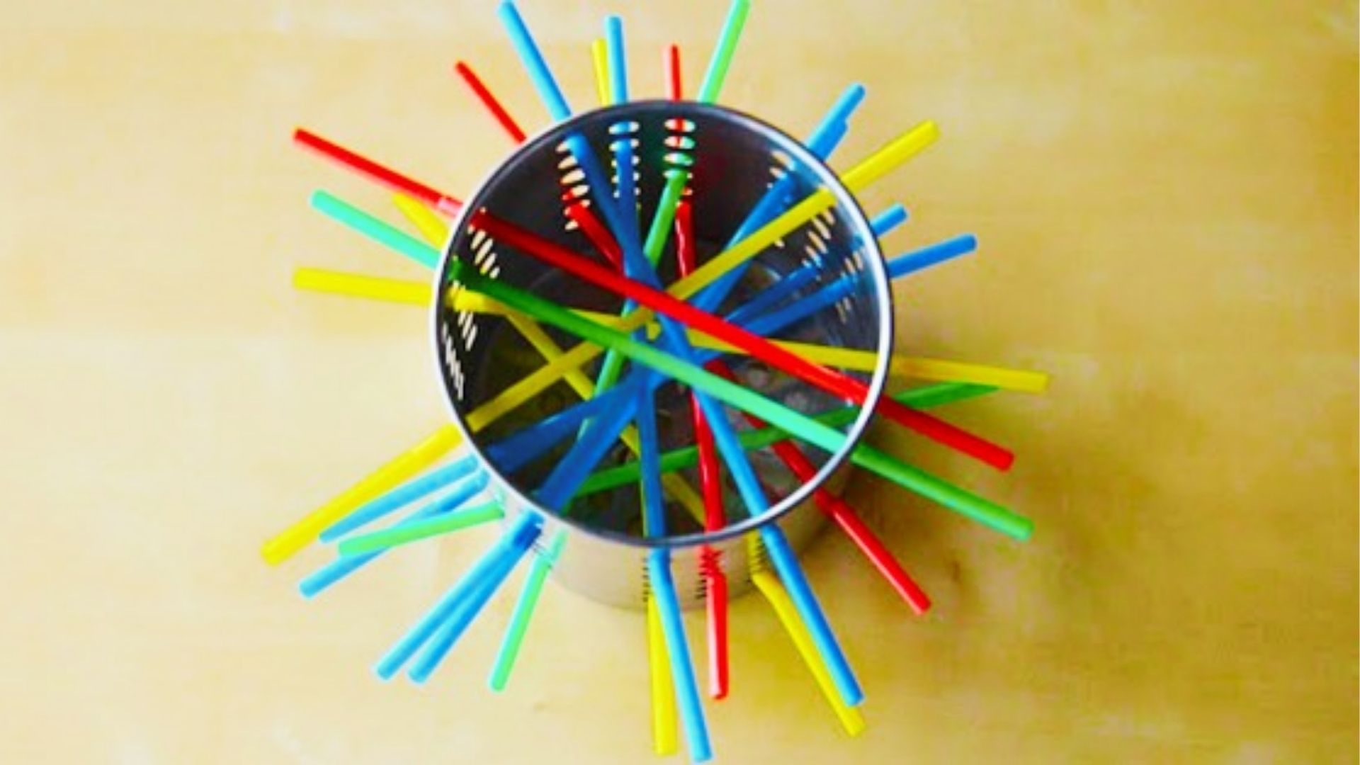 Colorful plastic straws in red, blue, green, and yellow stick out of a metal utensil holder like fireworks.