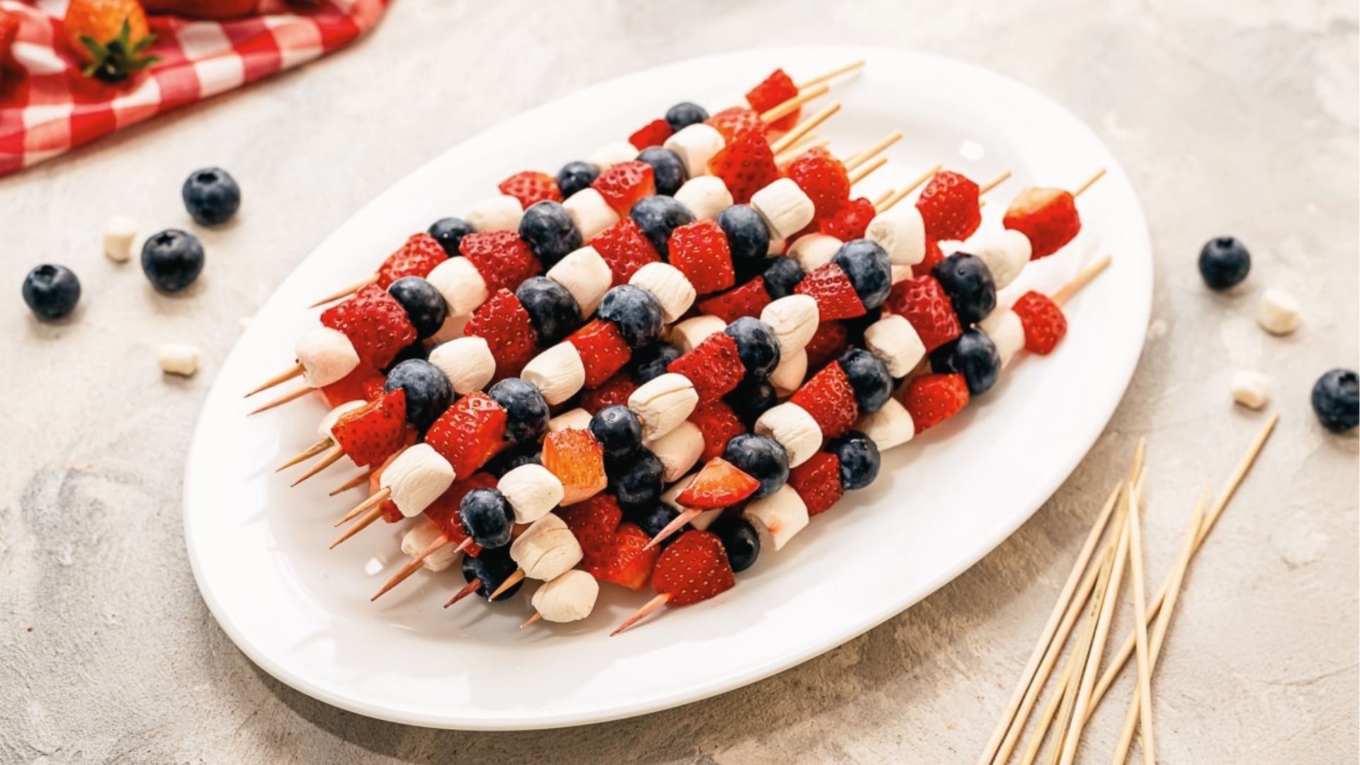 Fruit and marshmallow kabobs with strawberries, blueberries, and mini marshmallows on a white platter.