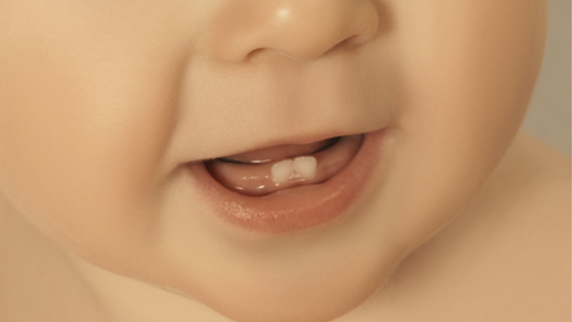 Close-up of a baby’s lower face and lips parted in a smile, highlighting two small bottom teeth.