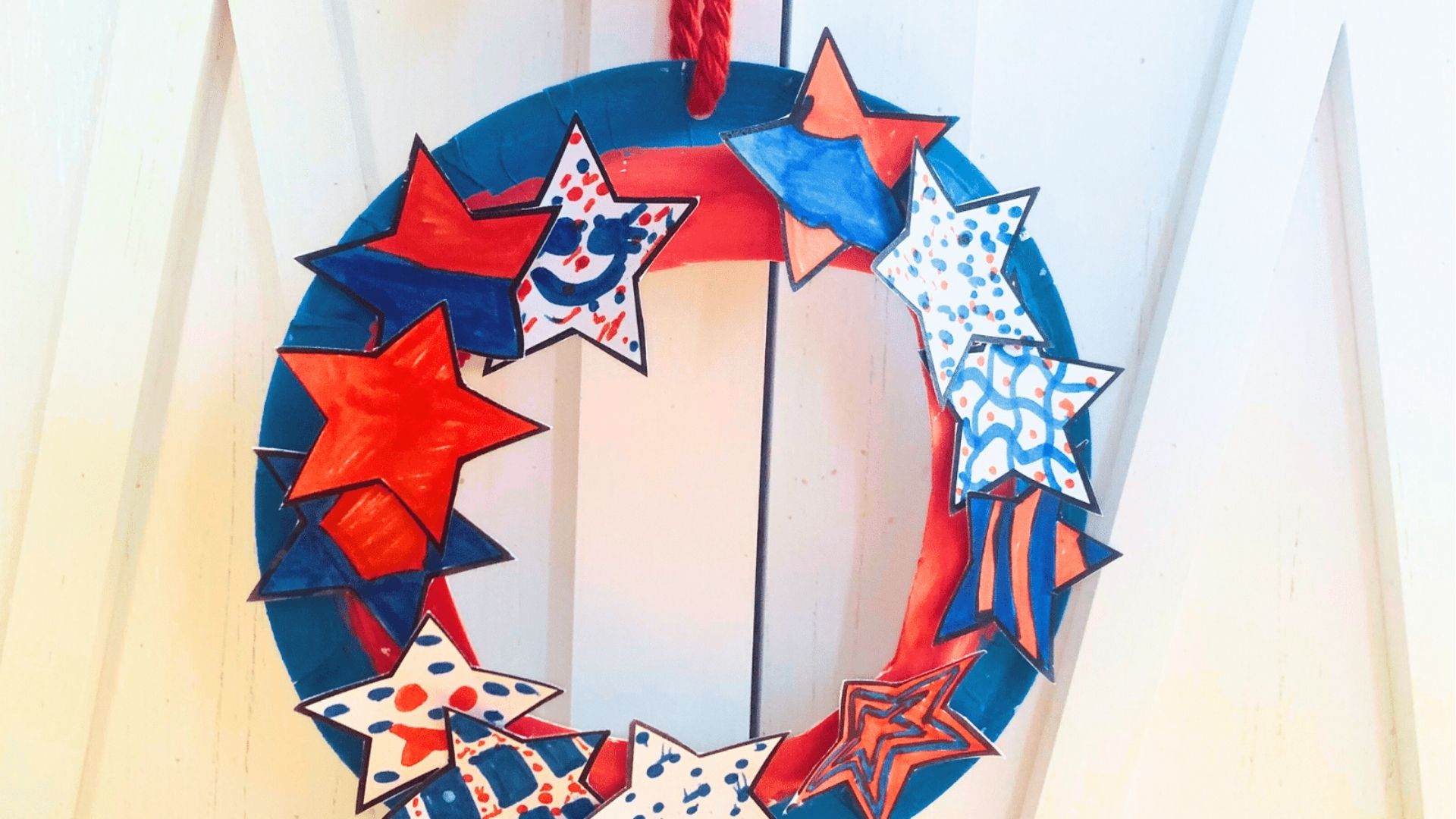 Paper plate wreath painted red and blue, covered with hand-colored star cutouts hanging on a white door