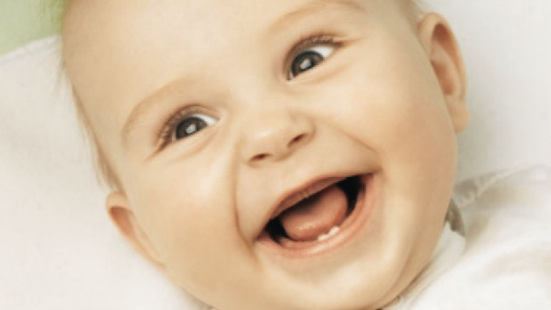 Smiling baby lying down showing a single bottom tooth just breaking through the gum.