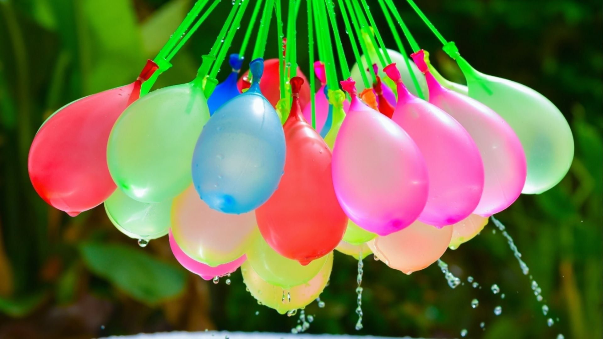 Bundle of colorful water balloons in red, blue, pink, and green dripping with water outdoors.