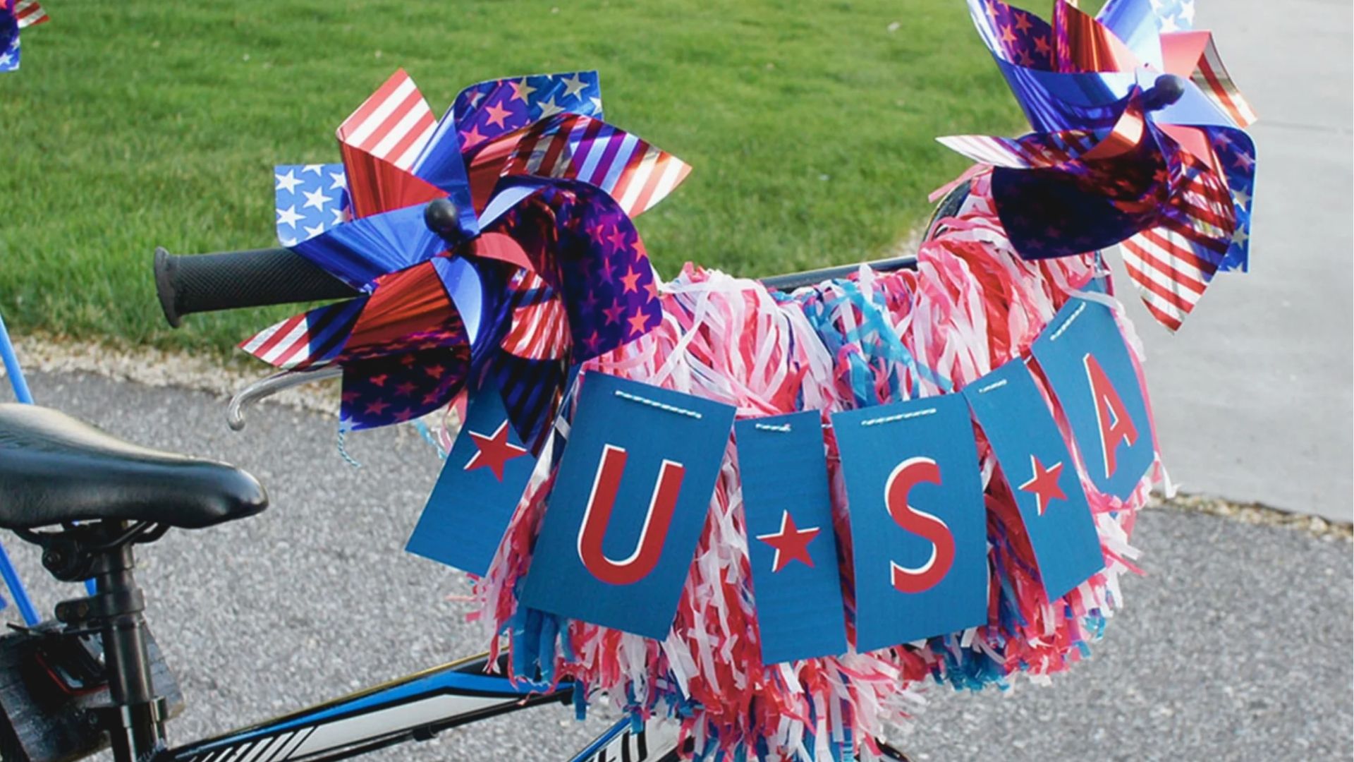 Close-up of a toddler bike decorated with patriotic pinwheels, red white blue streamers, and a USA banner.