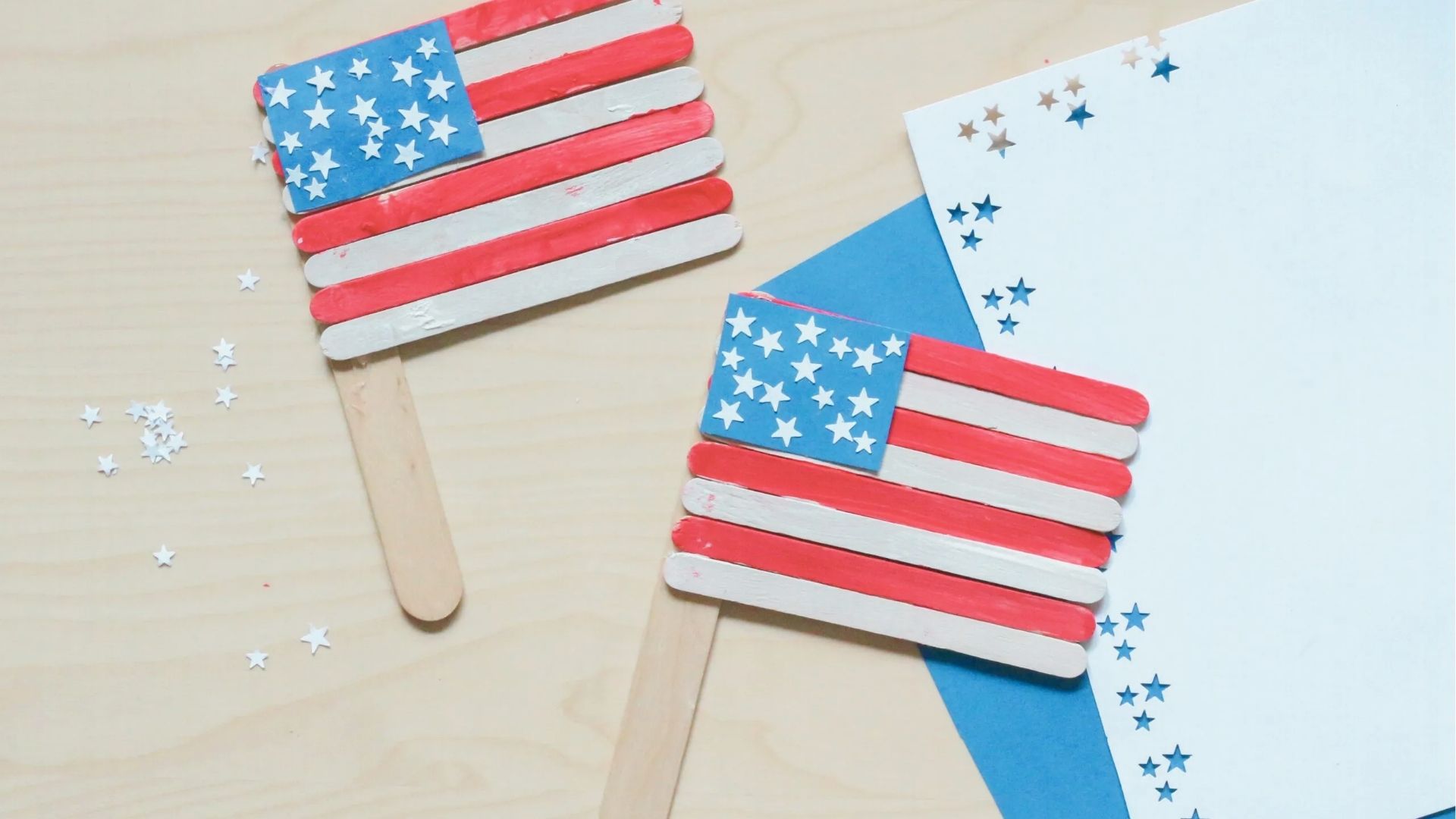 Two popsicle stick American flags with red and white painted sticks and blue squares with white star stickers