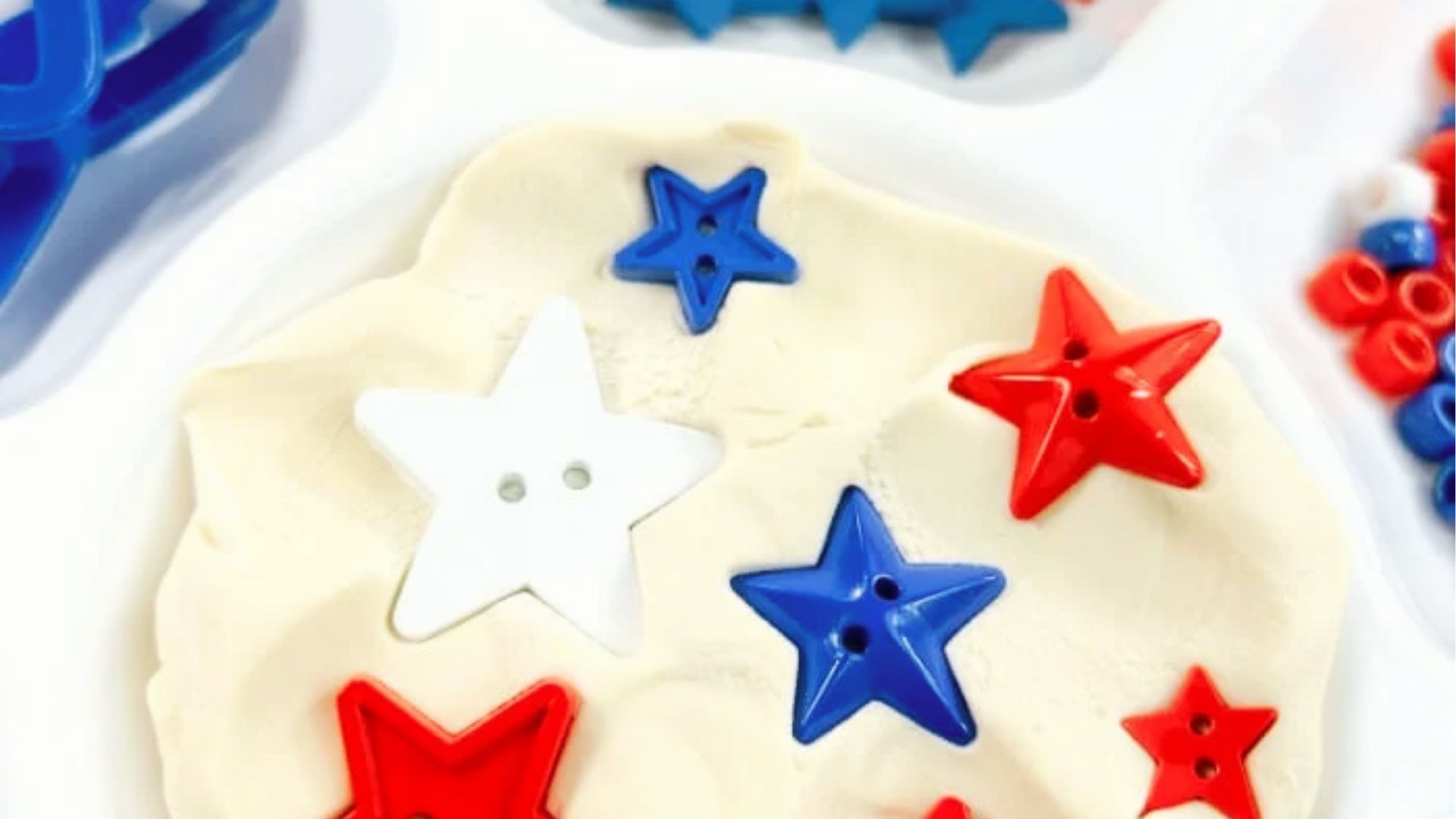 Red, white, and blue star buttons arranged on white playdough for a 4th of July theme.