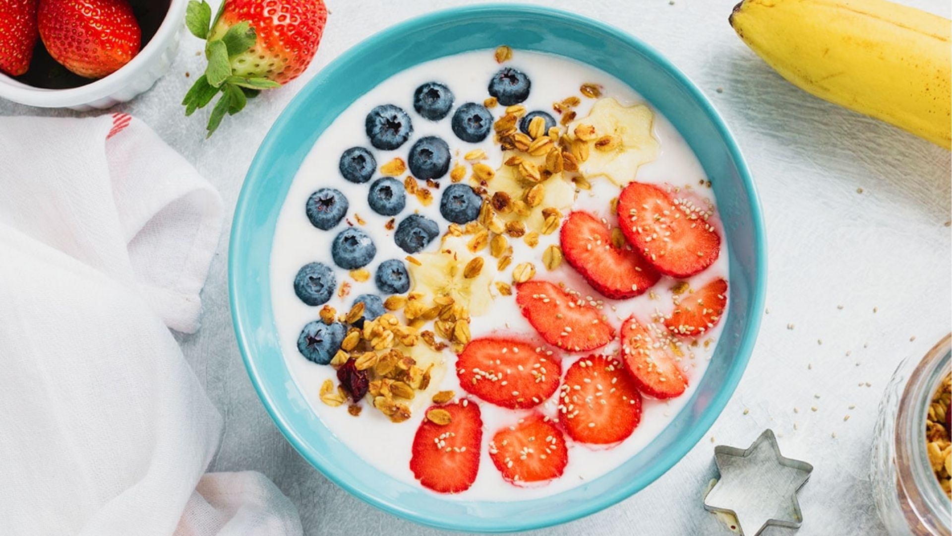 Teal bowl of yogurt topped with blueberries, strawberries, star-shaped banana slices, and granola.