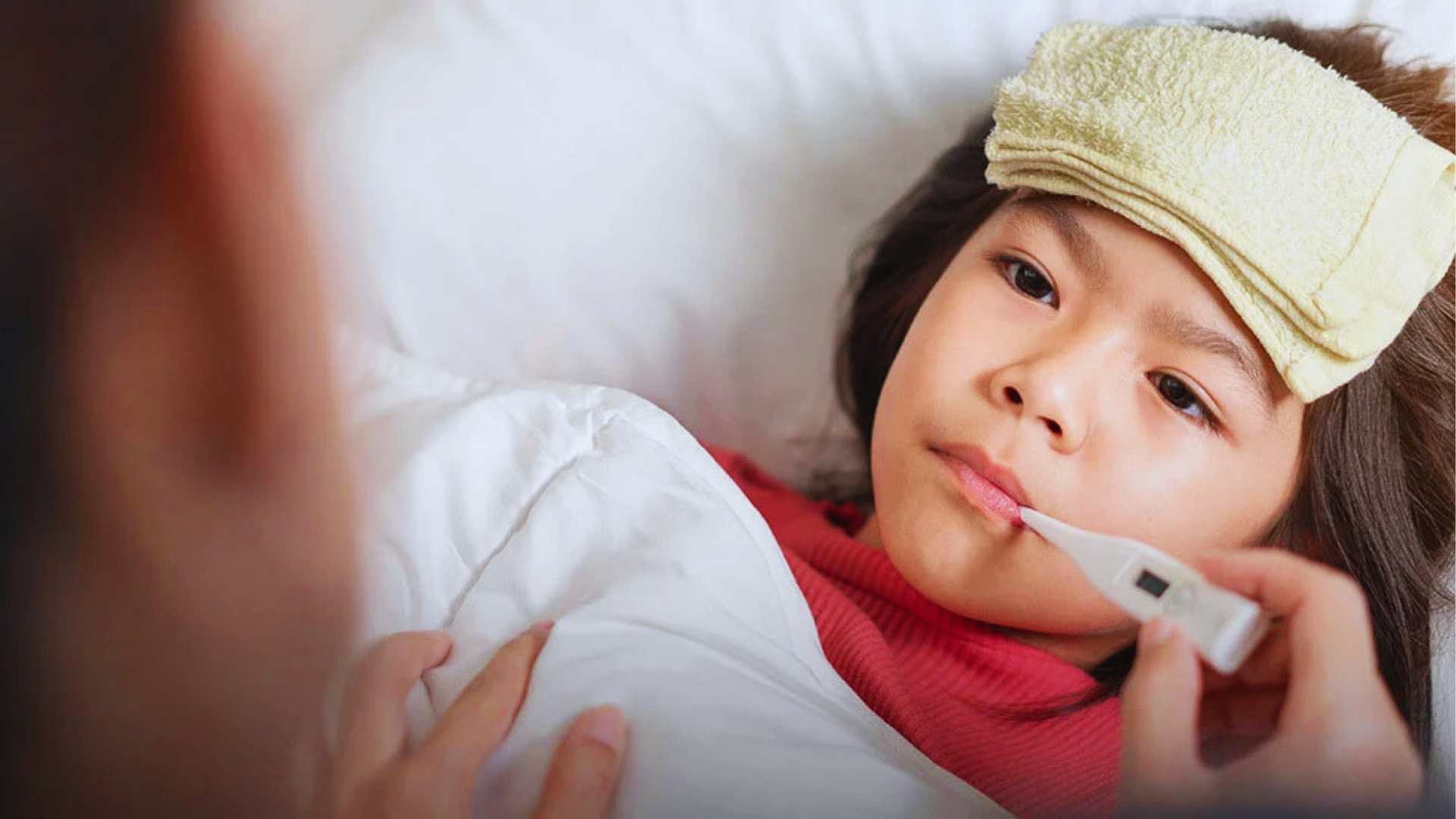Toddler girl with cool compress and thermometer in mouth, illustrating nighttime fever checks parents do when temperature spikes