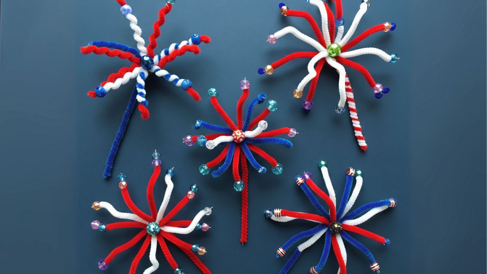 Five pipe cleaner fireworks in red, white, and blue with colorful beads on a dark blue background.