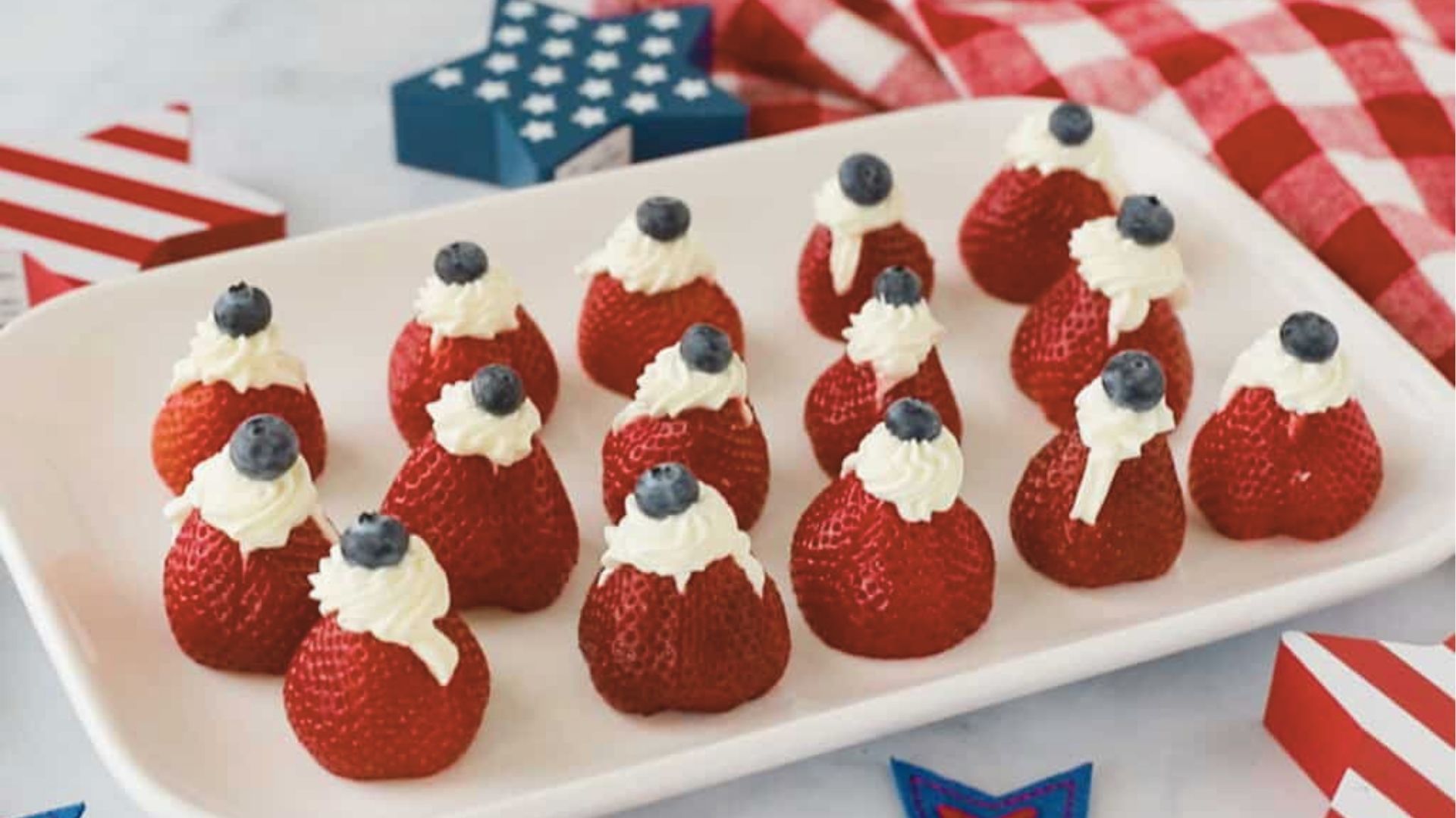 Strawberries filled with whipped cream and topped with blueberries sit on a tray with patriotic decor.