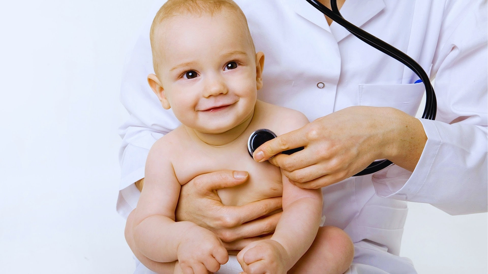Smiling baby getting pediatric checkup with stethoscope, showing routine doctor visits to discuss normal infant behaviors like head shaking.